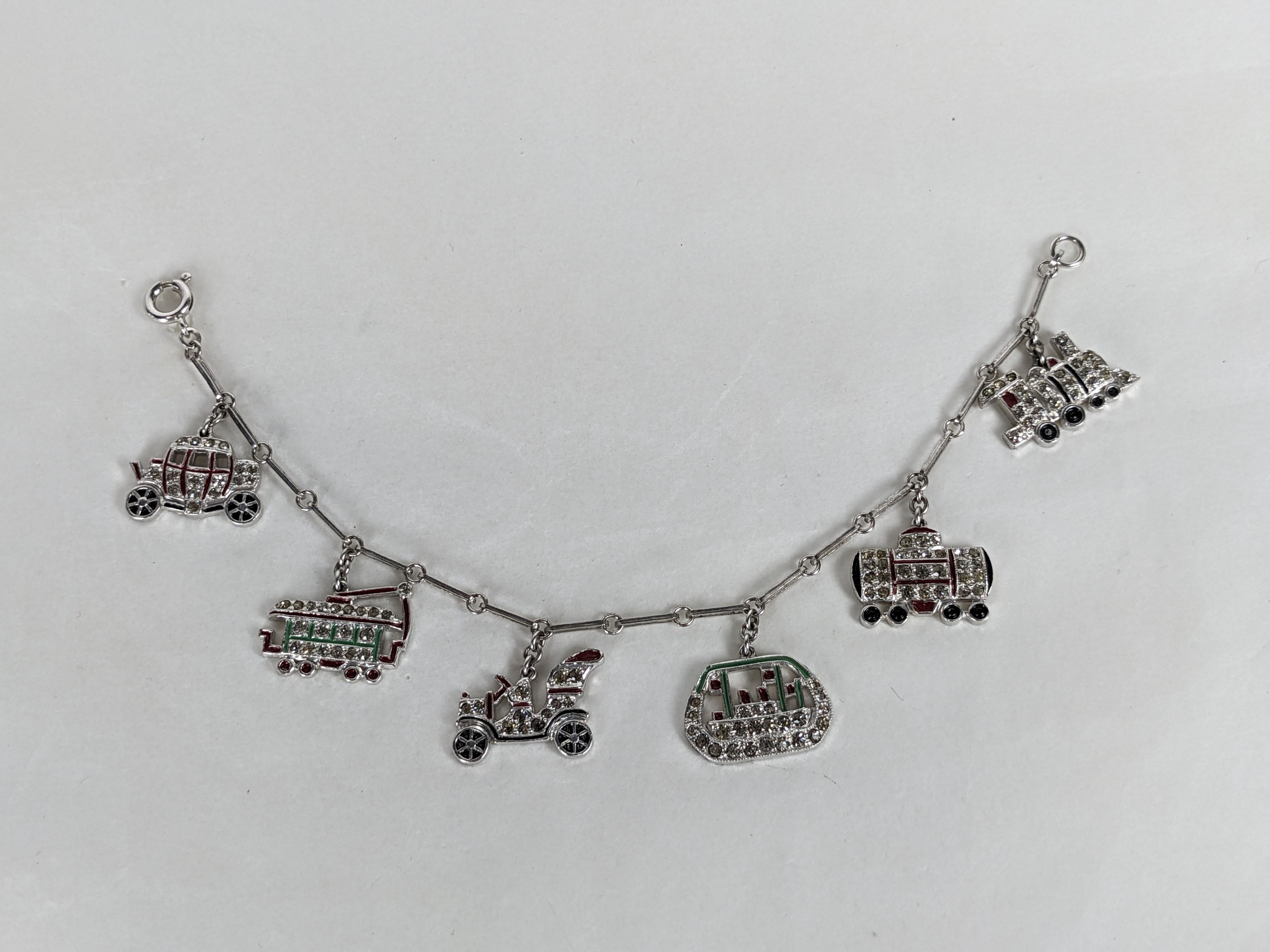 Bracciale Charm Figurale Art Deco degli anni '30. Charme a tema trasporti in metallo rodiato con accenti di smalto e pave di cristalli. Gli charme includono una carrozza, dei treni, un calesse e un battello a vapore. Alta qualità simile a quella di