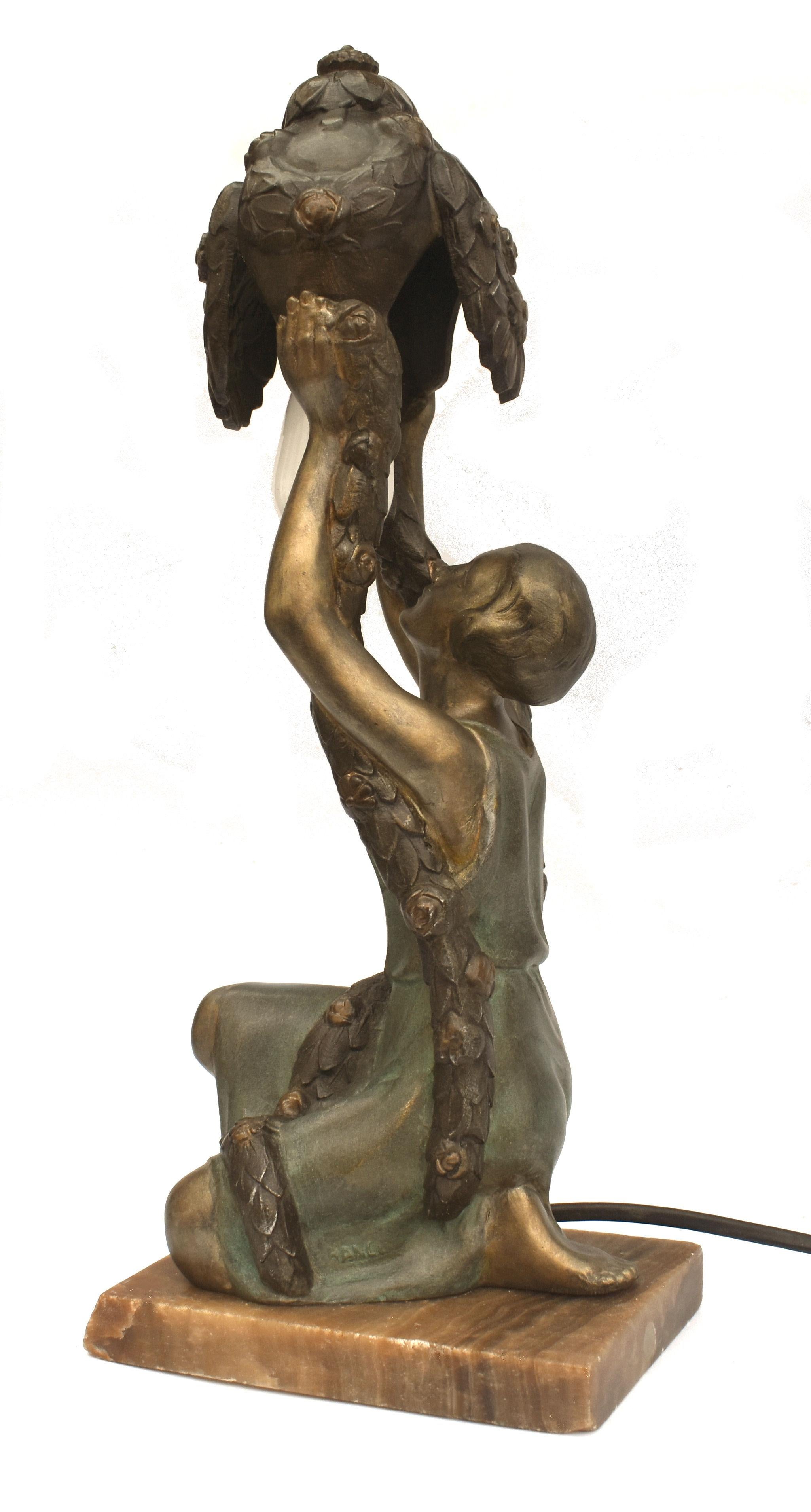 D'une hauteur impressionnante de 34 cm, cette lampe de table originale en étain peint à froid des années 1930 est signée P. Sega, France, et représente une jeune femme tenant en l'air un feuillage. Agenouillée sur un socle d'onyx, elle est en très