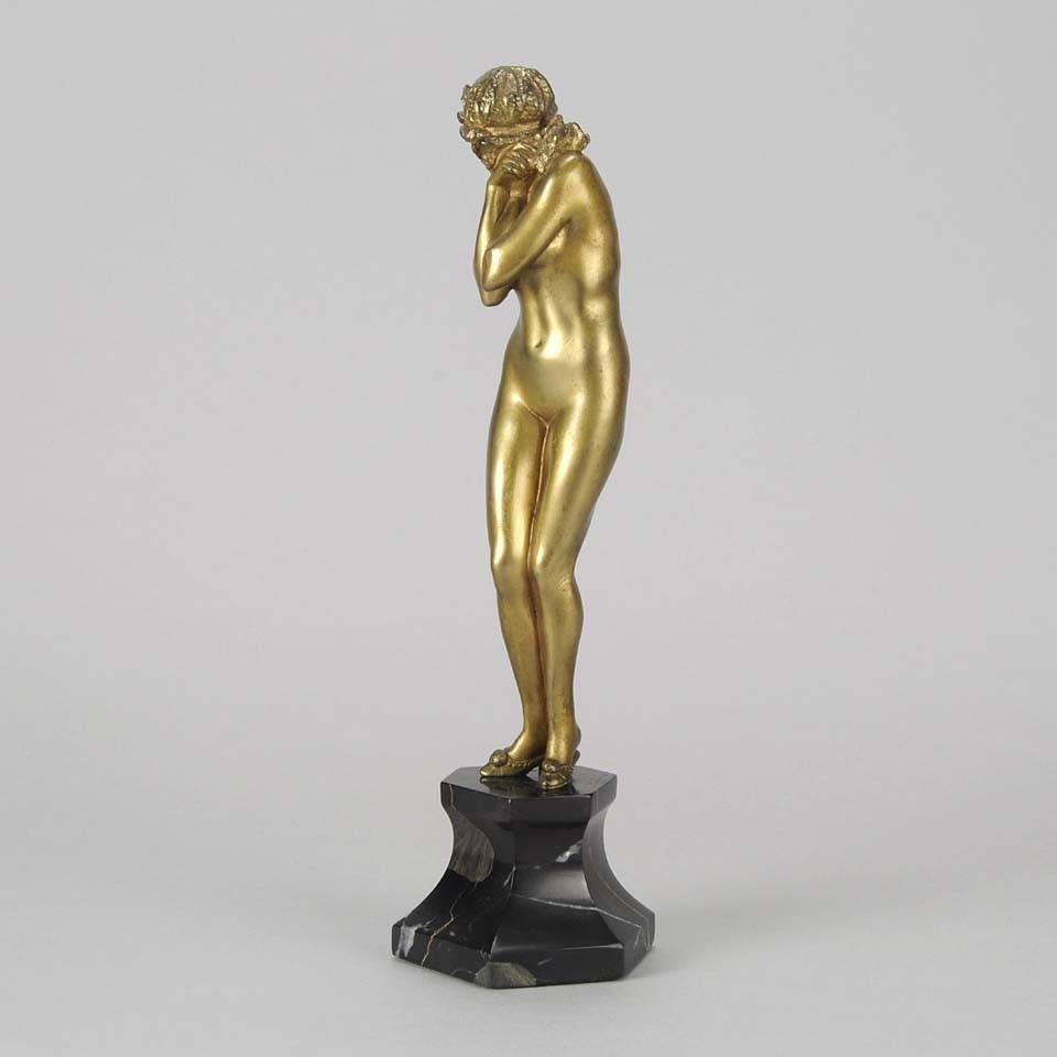 An excellent cold painted bronze study of a young beauty, standing naked except for her heeled slippers, in a coy pose covering her modesty with her crossed arms. The bronze with fine deep golden color and good hand finished detail, raised on a