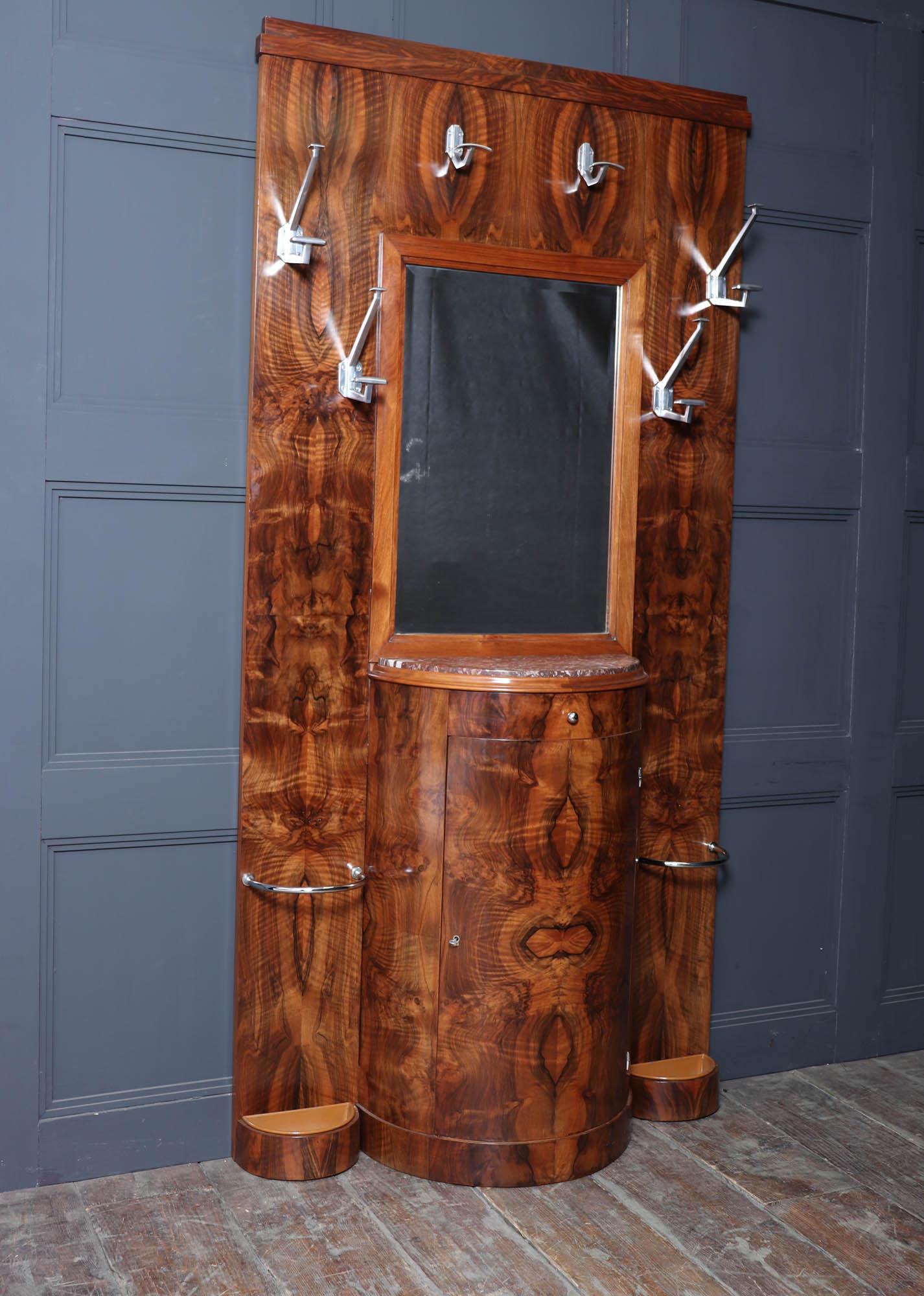 A tall and elegant Art Deco hall stand, crafted in beautifully figured walnut with chrome fittings and mirror, dating to the 1930s. This striking piece combines practical functionality with the bold, glamorous style of the period.

The design