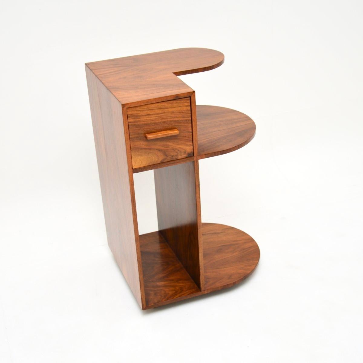 A stunning and quite unusual Art Deco figured walnut side table. This was made in England, it dates from the 1930’s.

It has a stylish and useful design, there is a single drawer and three open shelving spaces. This is nicely finished on all sides