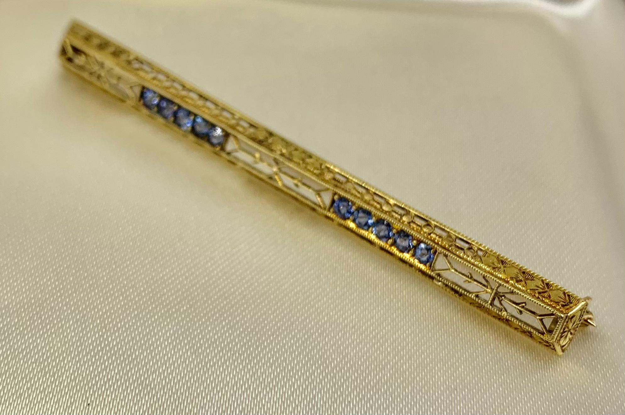 Beautifully intricate 14k yellow gold filligre bar brooch set with 10 medium blue sapphires approximately .3 TCW. The sapphires set in two lines of five gemstones flanked by elongated filigree sections with stylized arrow motifs, framed by a highly
