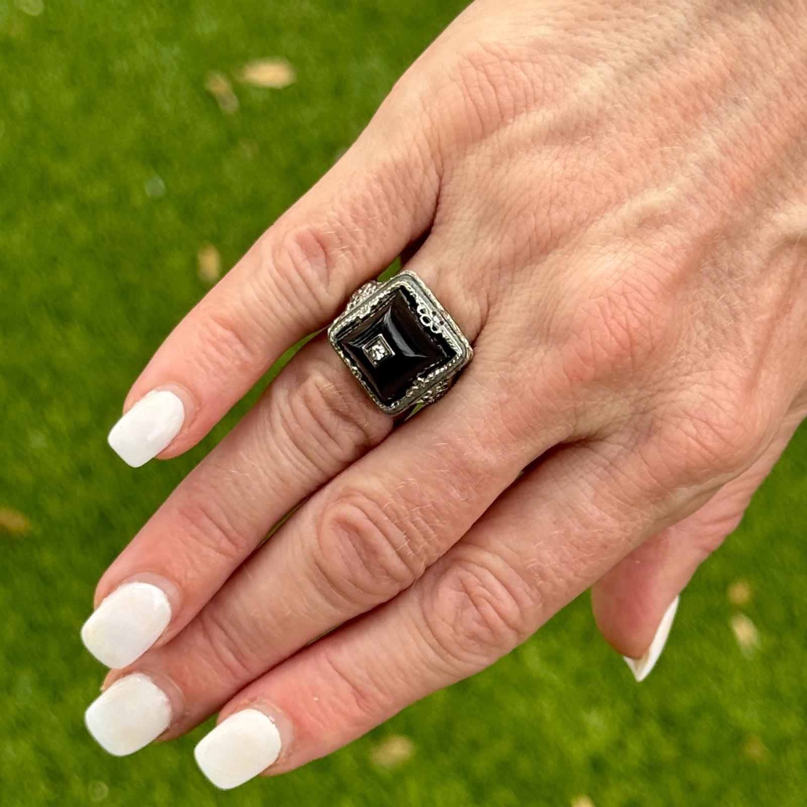 This stunning Art Deco ring is a masterpiece of vintage design, crafted in 14 karat white gold. The ring features an elegant dome shape, adorned with intricate filigree work that showcases the exceptional craftsmanship of the era. At the center of