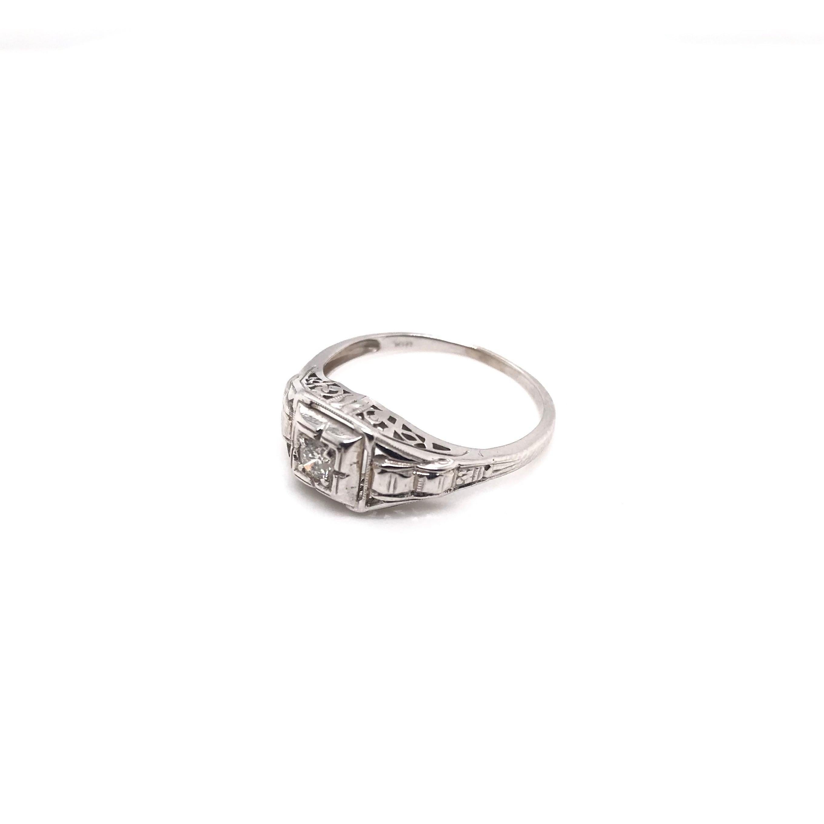 This antique piece was handcrafted sometime during the Art Deco design period ( 1920-1940 ). This antique ring features many charming details. The 18k white gold setting features a small sparkling diamond accent in the center. The ring has beautiful