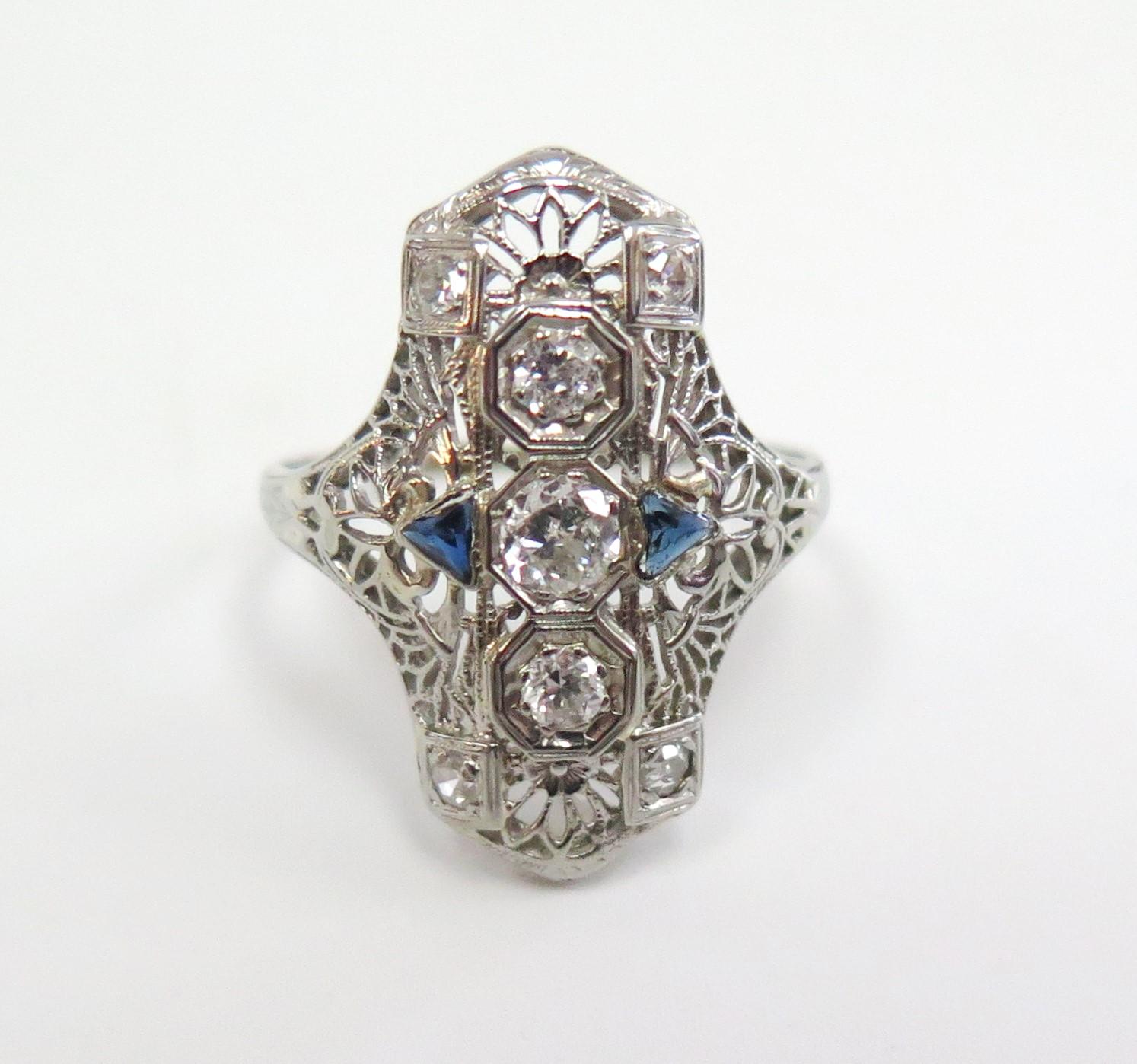 Three round Old European cut diamonds sparkle in a line with a Single Cut Diamond in each corner,  while genuine triangle-cut sapphires accent this detailed Art Deco filigree dinner ring. 

Total Diamond Weight: 0.42 Carat, Color: G-H, Clarity: