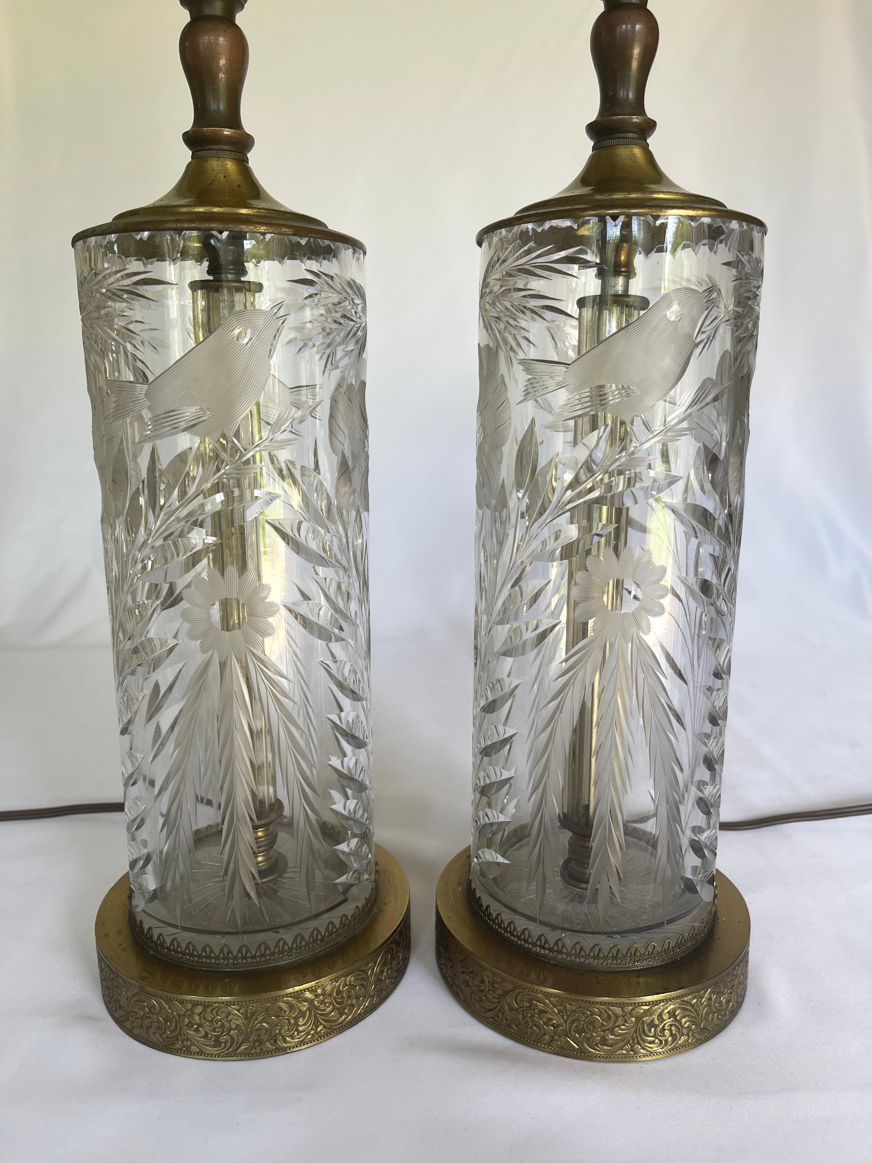 Art Deco finely detailed cut crystal cylinder lamps with floral and bird motifs, mounted on circular embossed brass bases. Interior cut crystal columns surround the lamp rods. 

The cut crystal lamp bodies measure 13