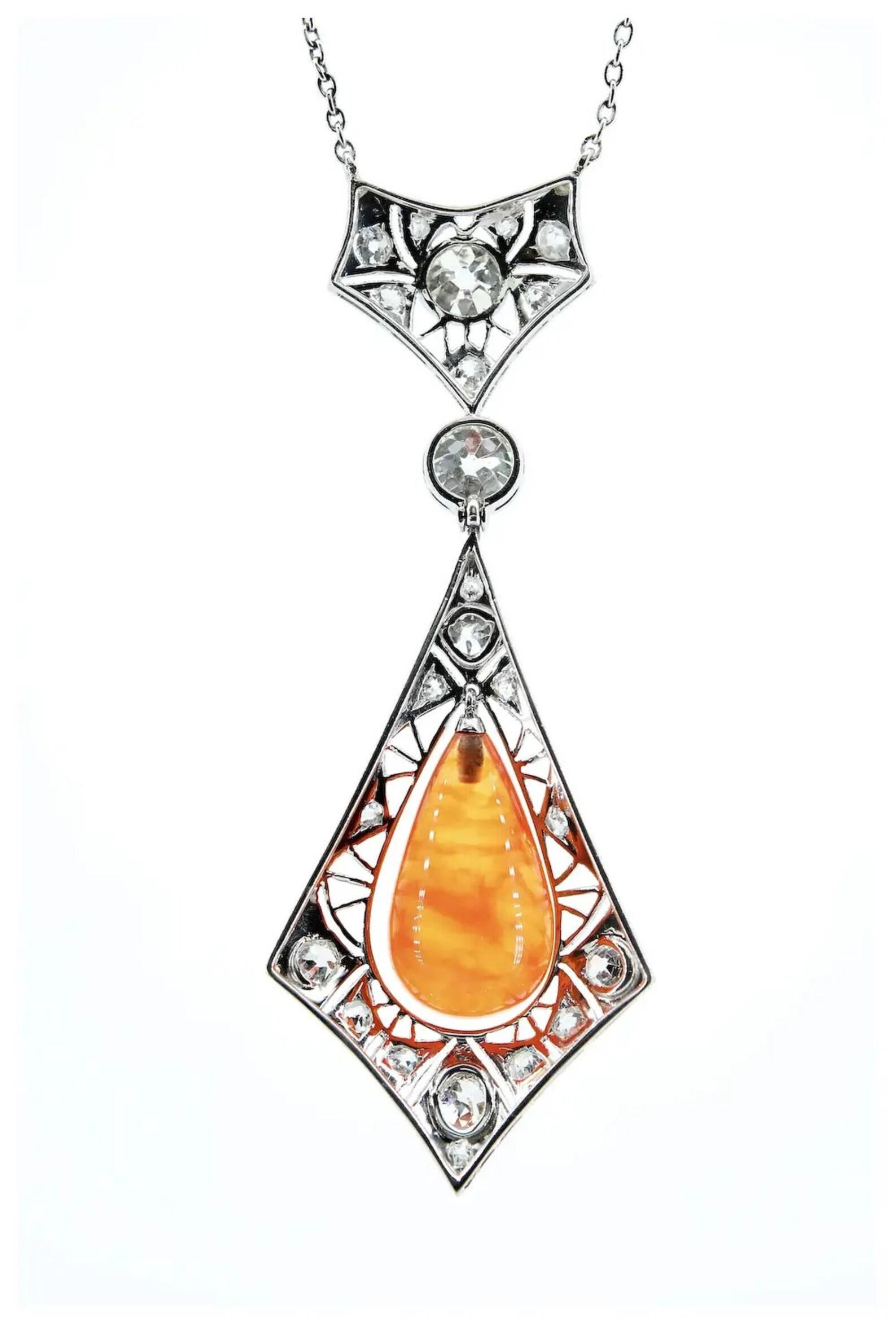 A One of a Kind Art Deco period Fire Opal and diamond pendant necklace in platinum.

Centered by an approximately 10.75ct Fire Opal displaying a beautiful golden orange color with excellent flash and translucency.

Complemented by a duet of bezel