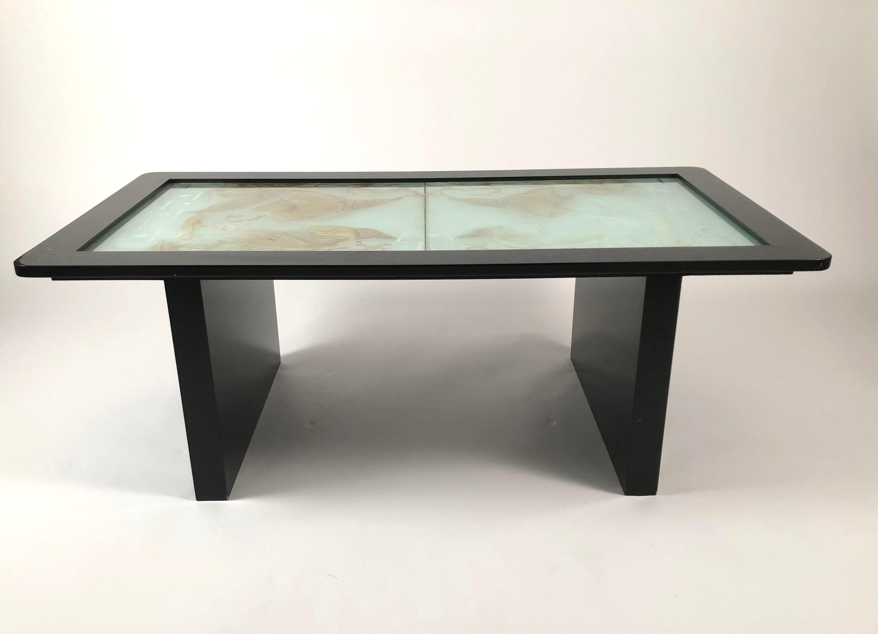 A coffee, or cocktail, table of rectangular form, with an Art Deco period etched and silver and gold highlighted glass top, in 2 panels, decorated with fish, coral and geometric bands and circles. The ebonized black lacquered frame and legs are very