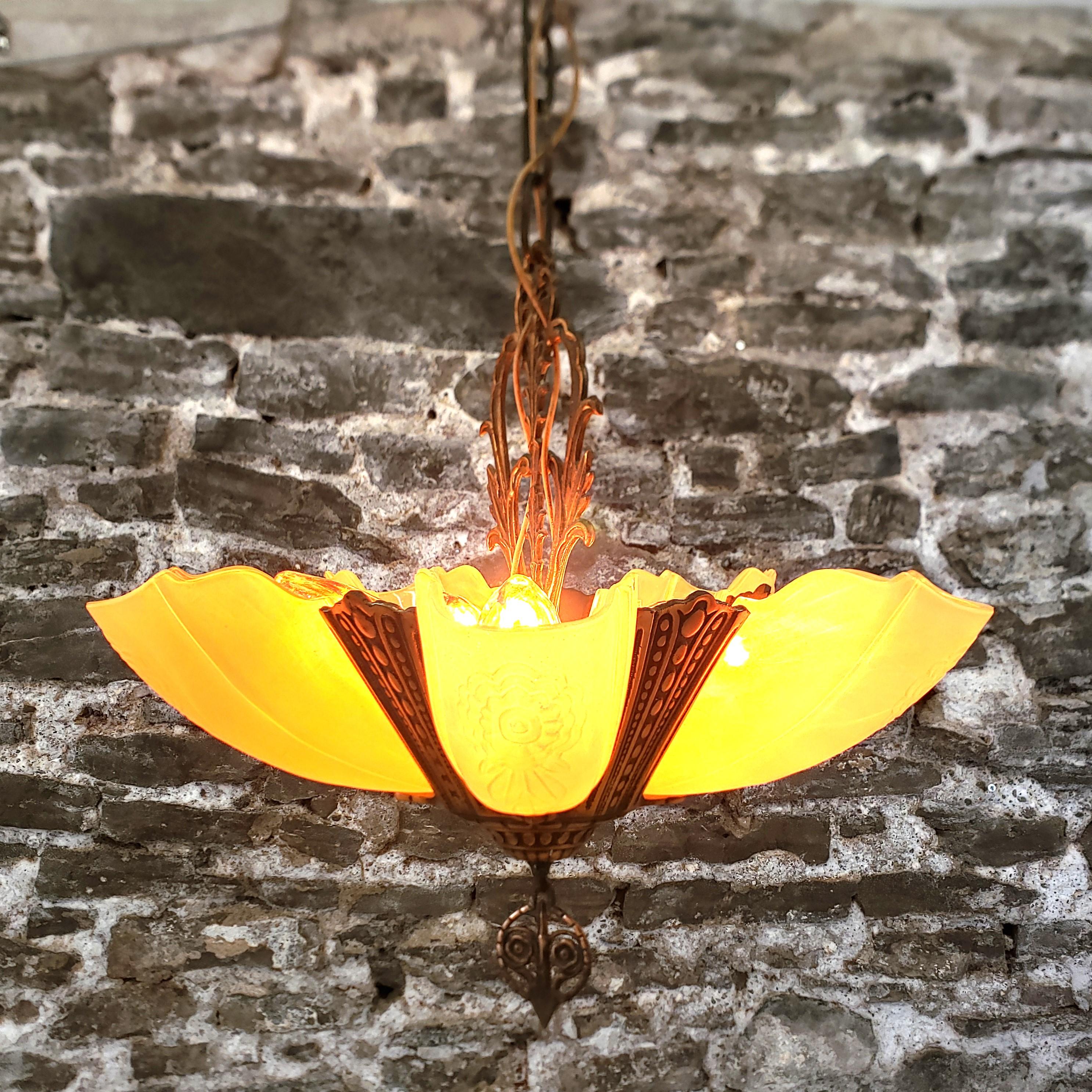 Esta lámpara de araña antigua fue fabricada por la Crown Lighting Company de Estados Unidos y data aproximadamente de 1920, en estilo Art Déco. La luminaria está hecha de metal fundido patinado en latón y cinco pantallas de cristal moldeado con
