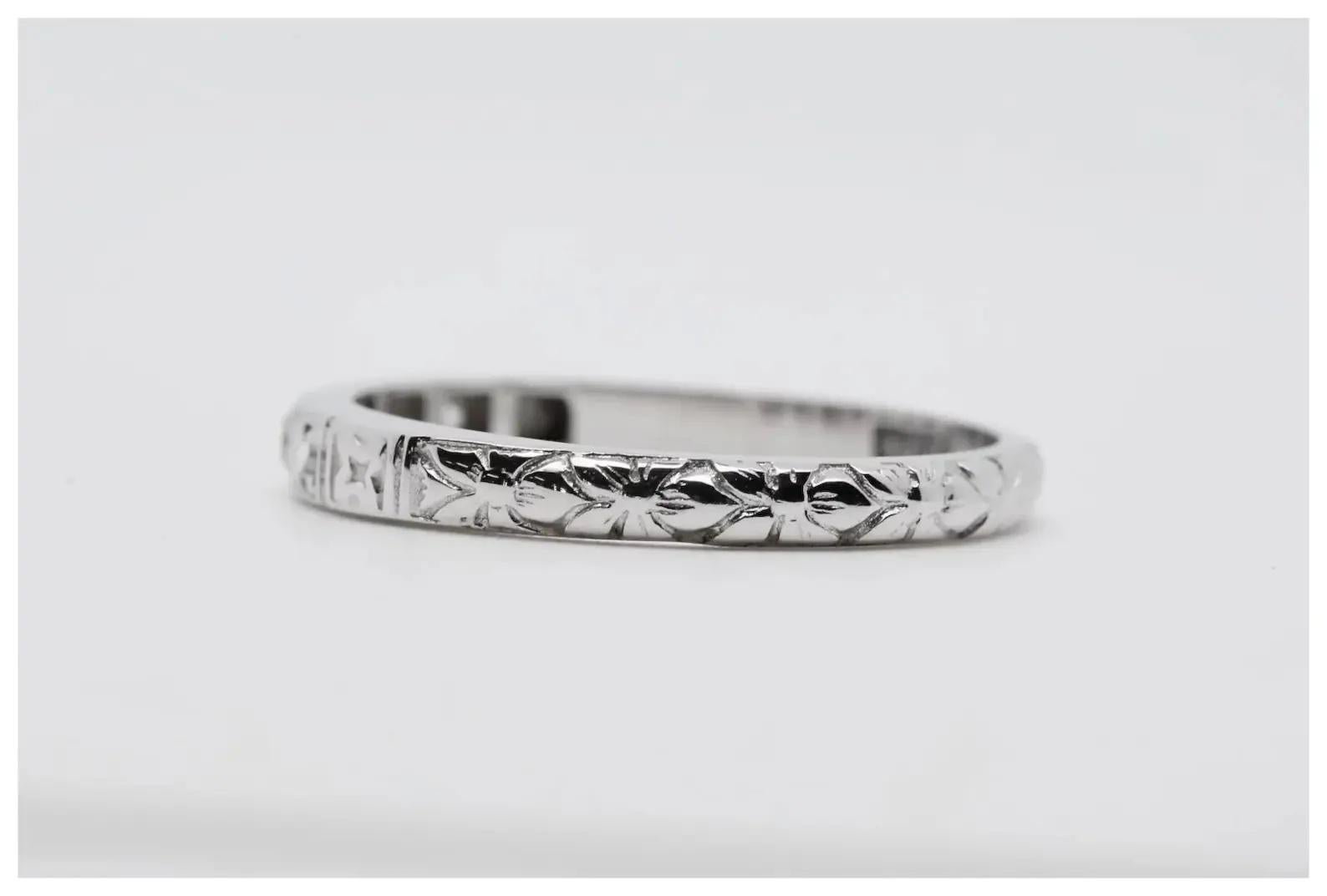 A handmade Art Deco period diamond wedding band in 18 karat white gold. Pave set with 5 round cut diamonds weighing a combined 0.10 carats and grading as H color, VS2 clarity. The band features hand engraved orange blossom flowers throughout in a