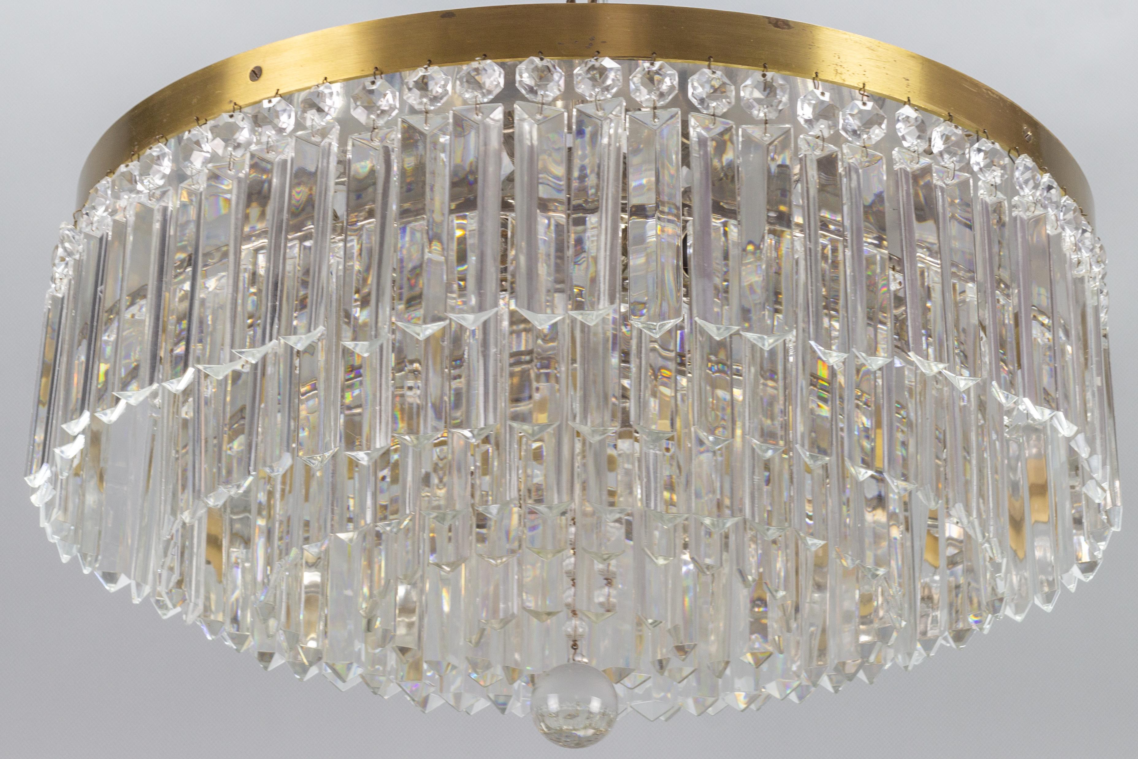 This impressive Art Deco style flush mount ceiling fixture in a classic wedding cake or waterfall form features five tiers of crystal prisms, terminating in a spherical glass ball in the center. The mounting base features a brass edge and a