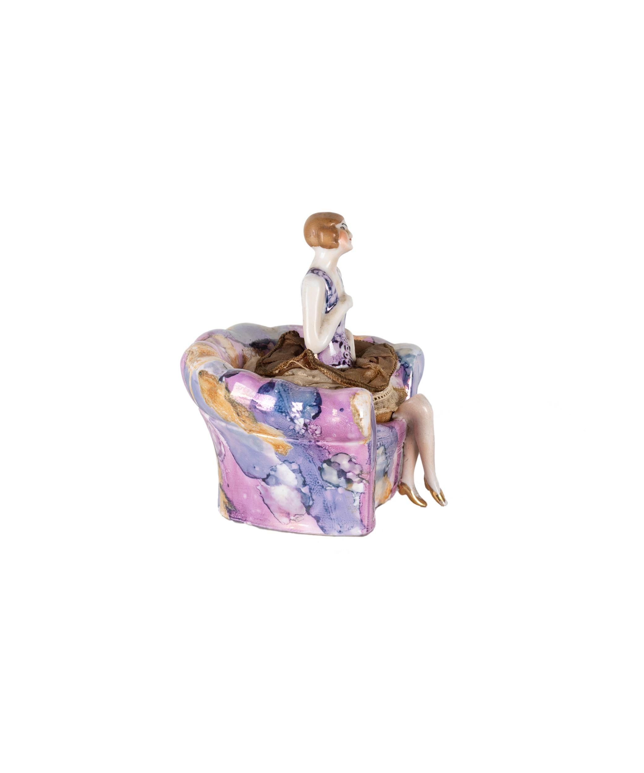 An Art Deco porcelain powder puff stand featuring a seated flapper lady with original puff, crafted in Germany by Carl Schneider circa 1920.

This whimsical piece captures the spirit of the Roaring Twenties. A brown-haired porcelain half-doll,