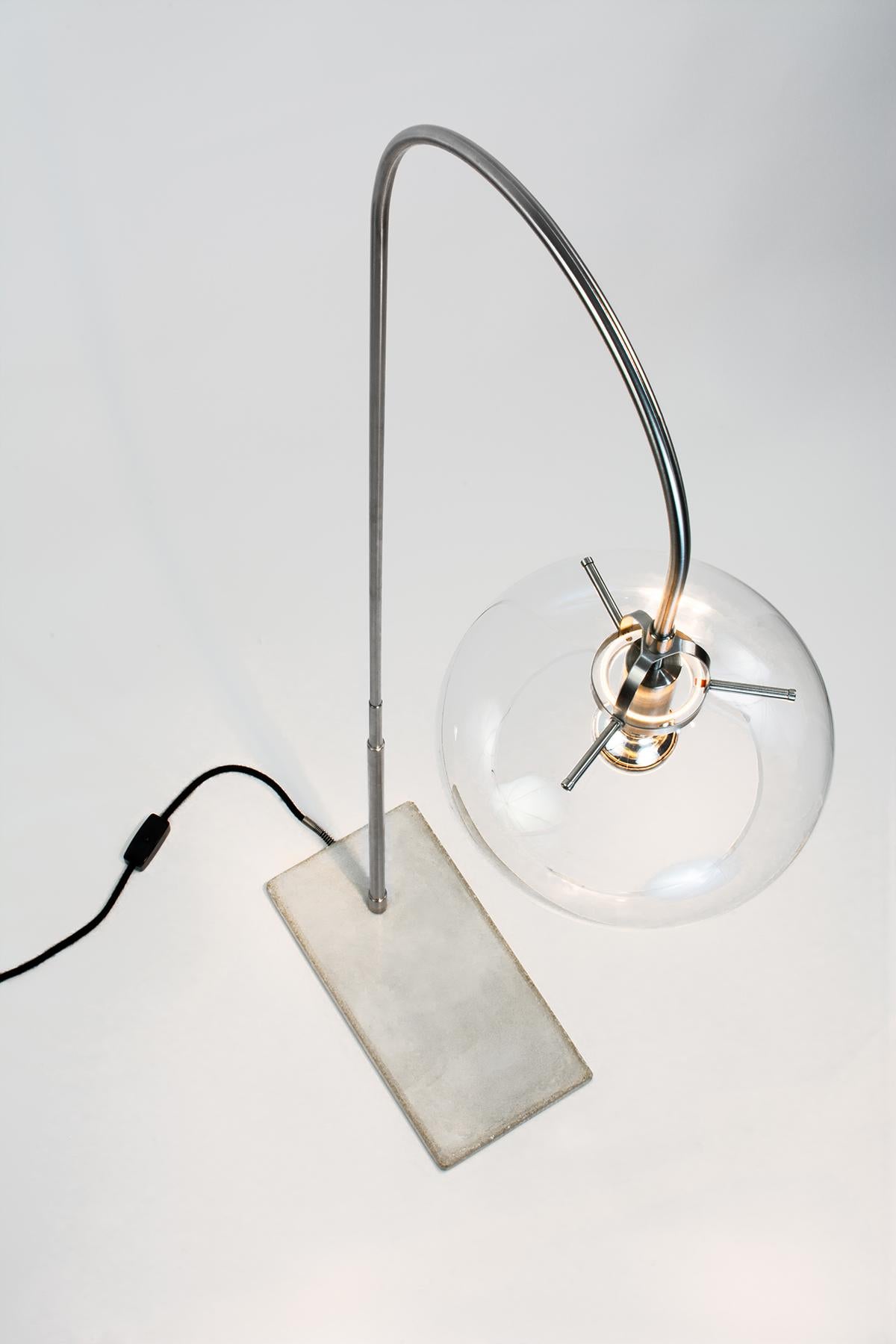 Ce remarquable lampadaire est un chef-d'œuvre d'inspiration Art déco qui ne manquera pas d'impressionner. La lampe se compose de composants élégants en acier inoxydable et d'un abat-jour en verre transparent, tandis que la base est construite en