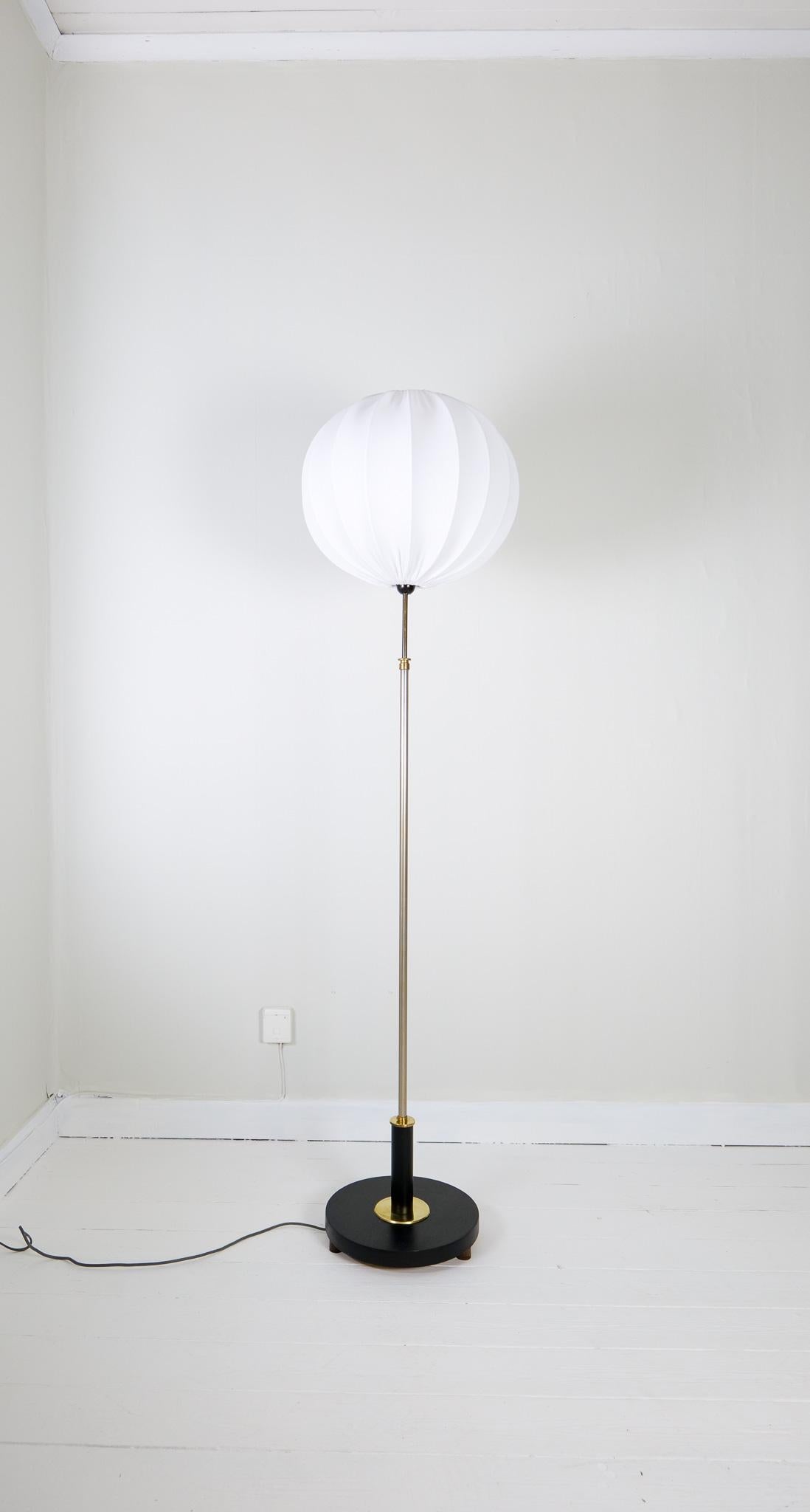 Art deco floor lamp made in a base of blackened wood and brass details with silver metal rod. The lamp can be adjustable in height. All around a good art deco looking floor lamp with a new round cotton shade.

Good vintage condition with some wear.