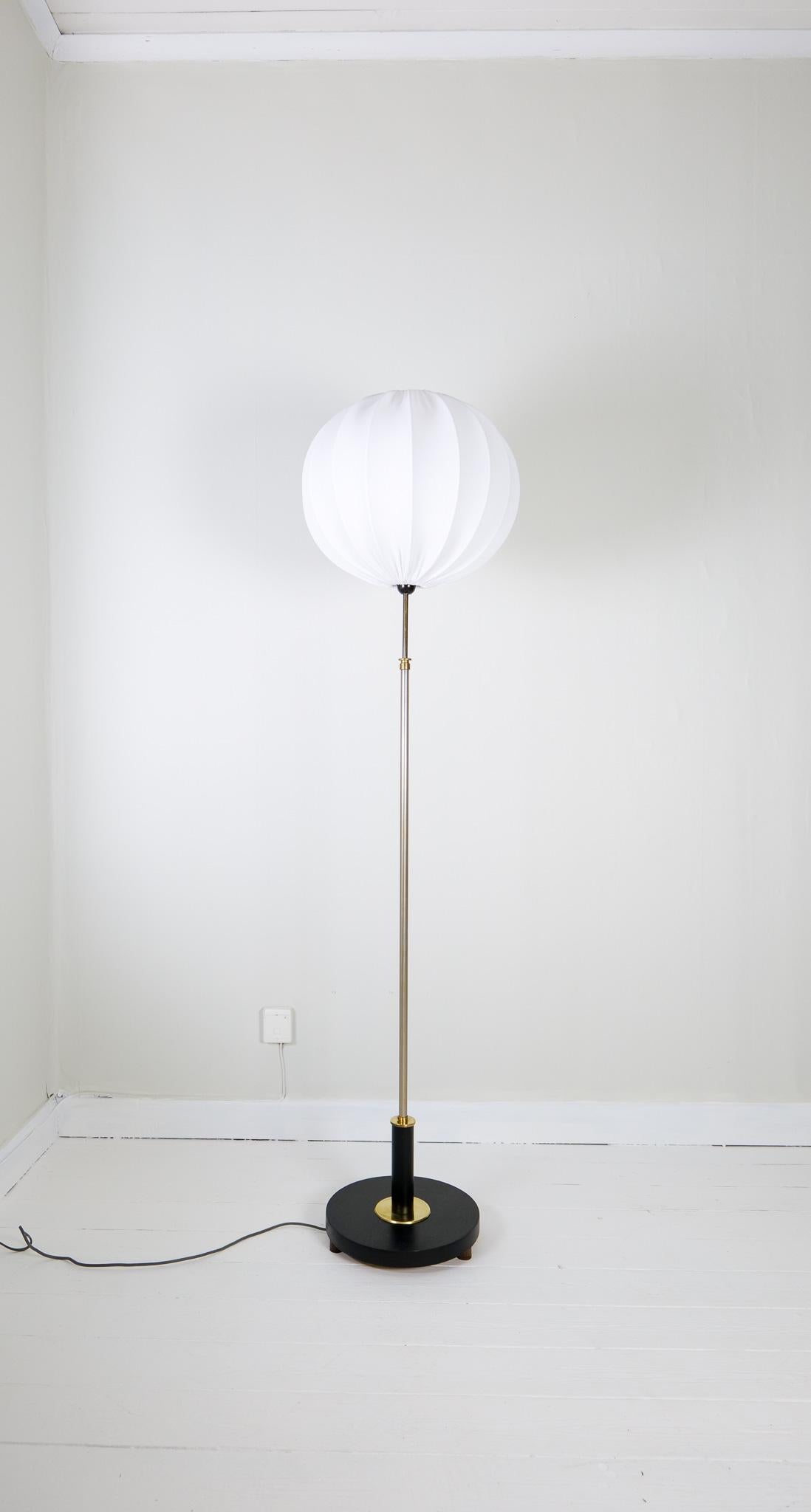 Lampadaire Art déco réalisé dans une base en bois noirci et détails en laiton avec tige en métal argenté. La lampe est réglable en hauteur. Un bon lampadaire art déco avec un nouvel abat-jour rond en coton.

Bon état vintage avec un peu d'usure.