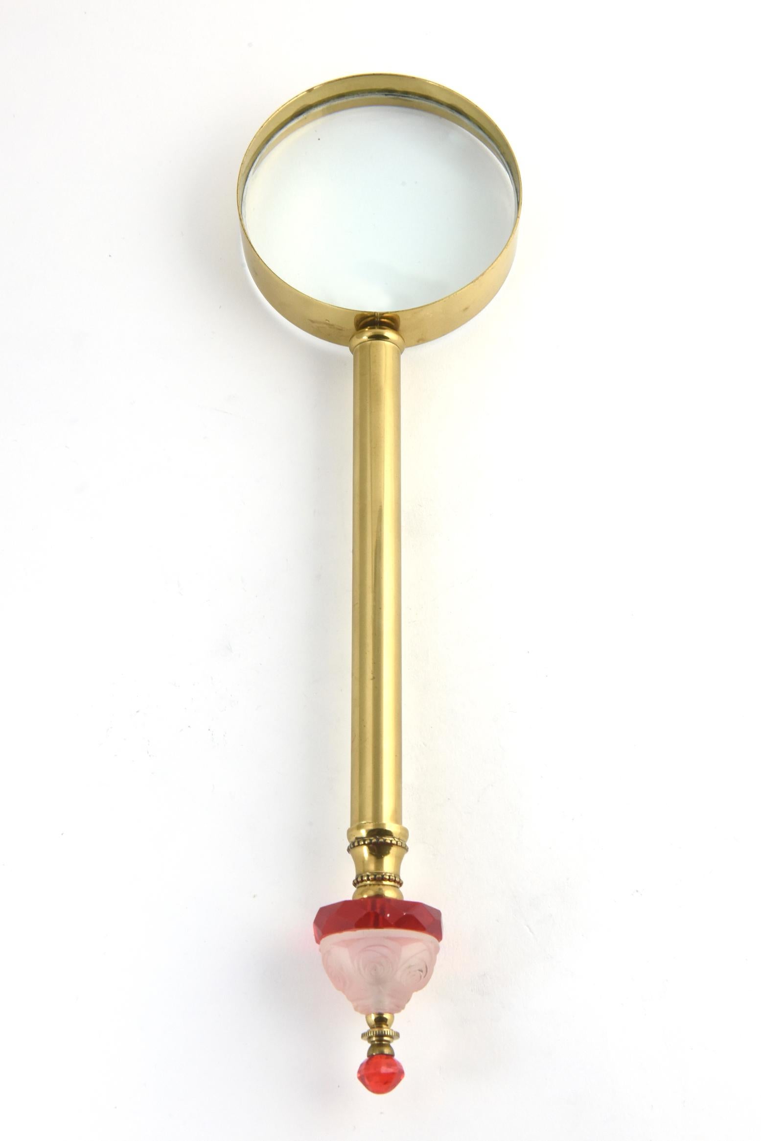Brass magnifier with red-and-white crystal accent piece on the handle. The center section is frosted crystal with raised floral design. On either side of the floral piece, there is a faceted red accent section. The magnifier portion is a later day