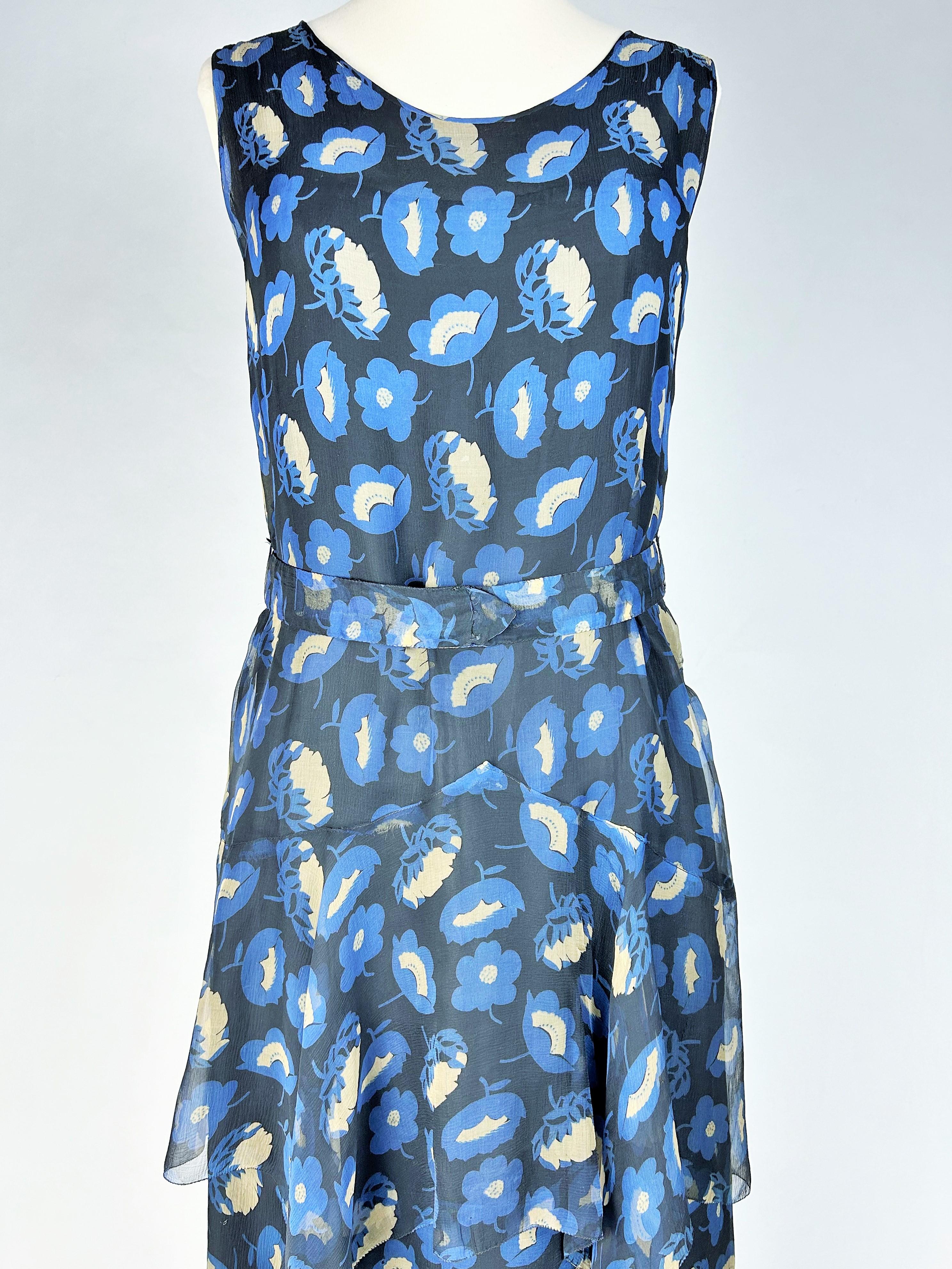 Hacia 1930-1935
Francia
Vestido largo de gasa de seda estampada con flores Art Déco azules y blancas sobre fondo negro, probablemente de Alta Costura y de los años 30. Vestido sin mangas con escote redondo rematado con ribetes. Típico corte tubular