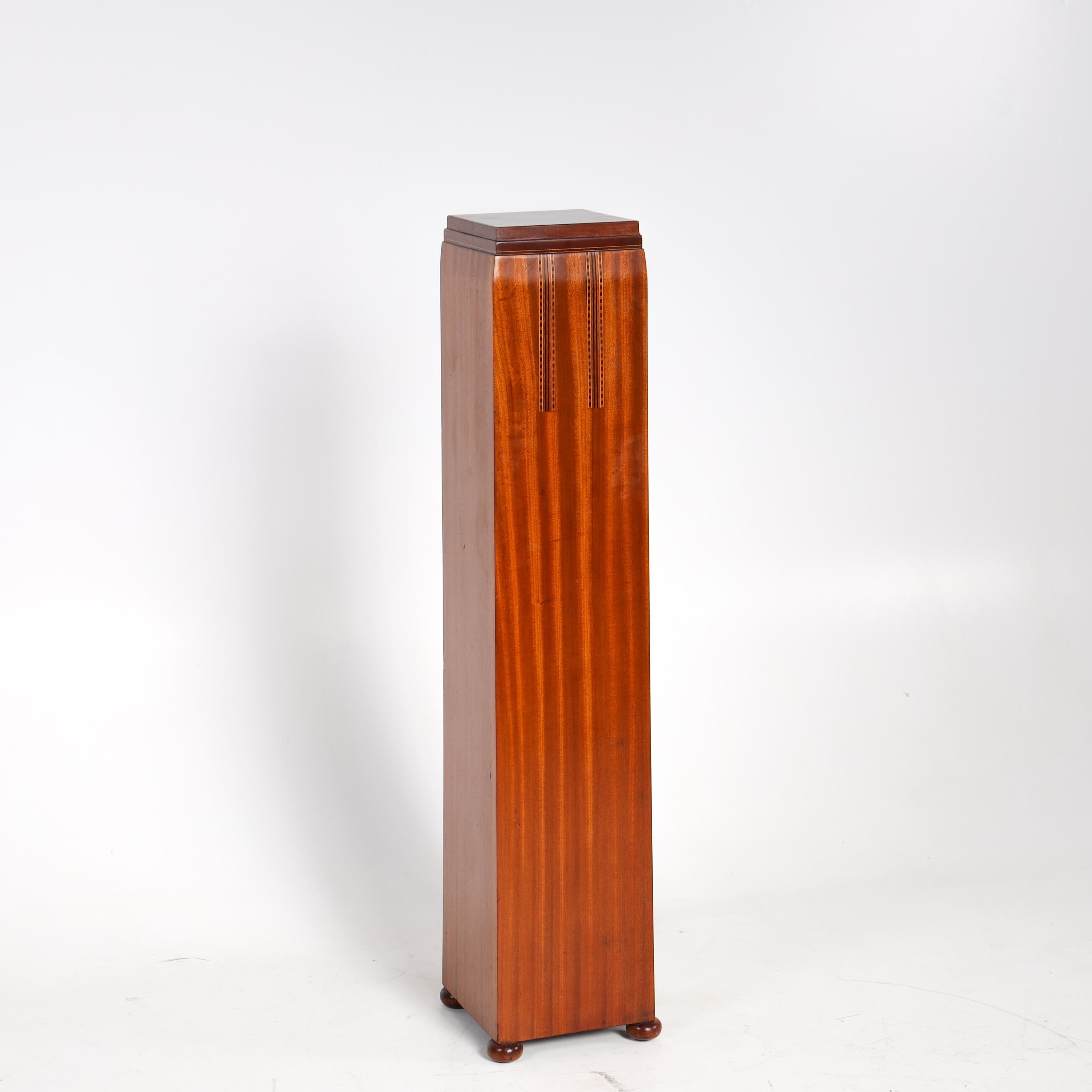 Art Deco column, standing on small bun feet, slightly tapering towards the top, with a square base and stepped platform. The front is decorated with two vertical inlays. Hand-polished.