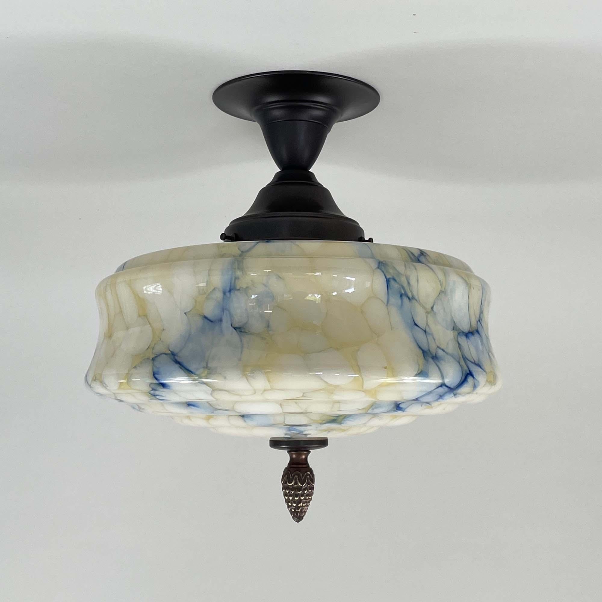 This Art Deco light fixture was designed and manufactured in Germany in the 1920s to 1930s during the Bauhaus period. It features a blue and cream  colored opaline glass lampshade with marbled, mottled decor and stepped design and bronzed /