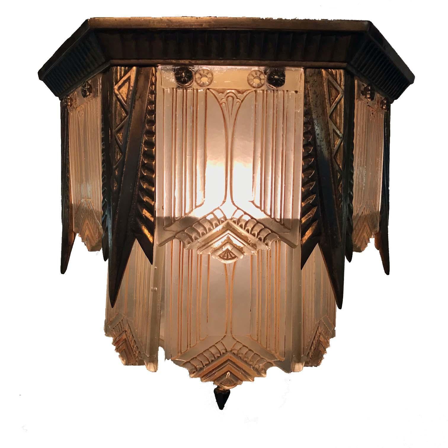 Esta linterna de vestíbulo americana con paneles de cristal empotrados es una rara supervivencia del periodo Art Déco. Del detallado marco hexagonal de bronce de dos niveles cuelgan los paneles de vidrio esmerilado moldeado, cada uno sostenido por