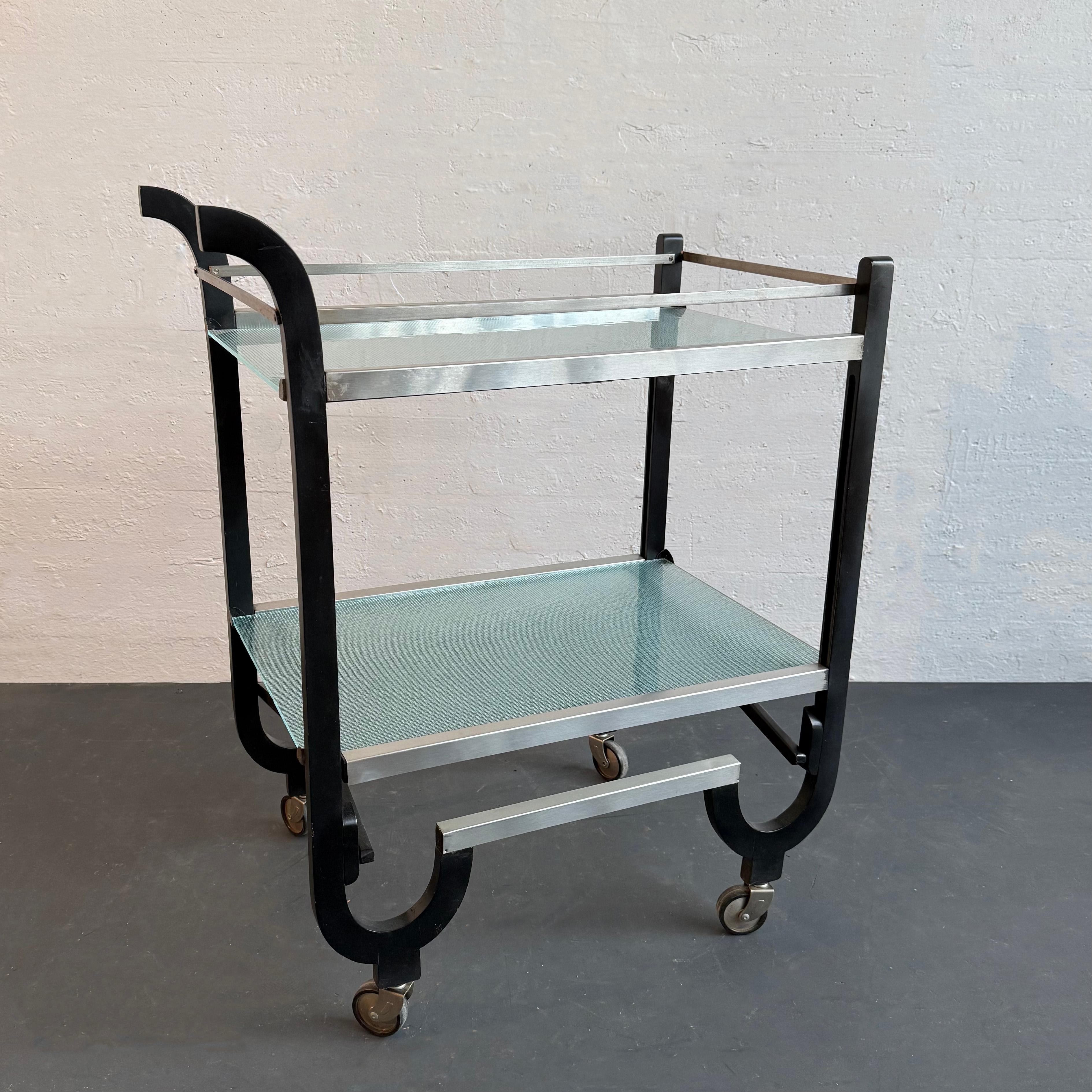 This stunning, American-made Art Deco, folding bar serving cart is attributed to the American Designer Donald Deskey.  Simply elegant with its black lacquered wood frame and aluminum trim, this 1930's rolling, collapsible modern cart features two