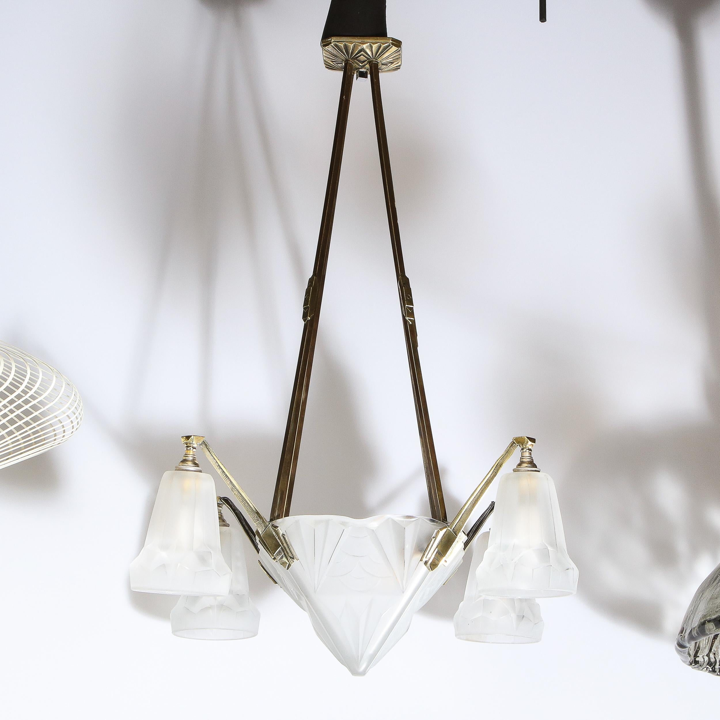 This elegant Art Deco chandelier was realized in France circa 1930. It offers a silvered bronze frame with a pyramidal body and four conical shades that descend from the cantilevered arms. The frosted glass of the body and shades is etched in bas