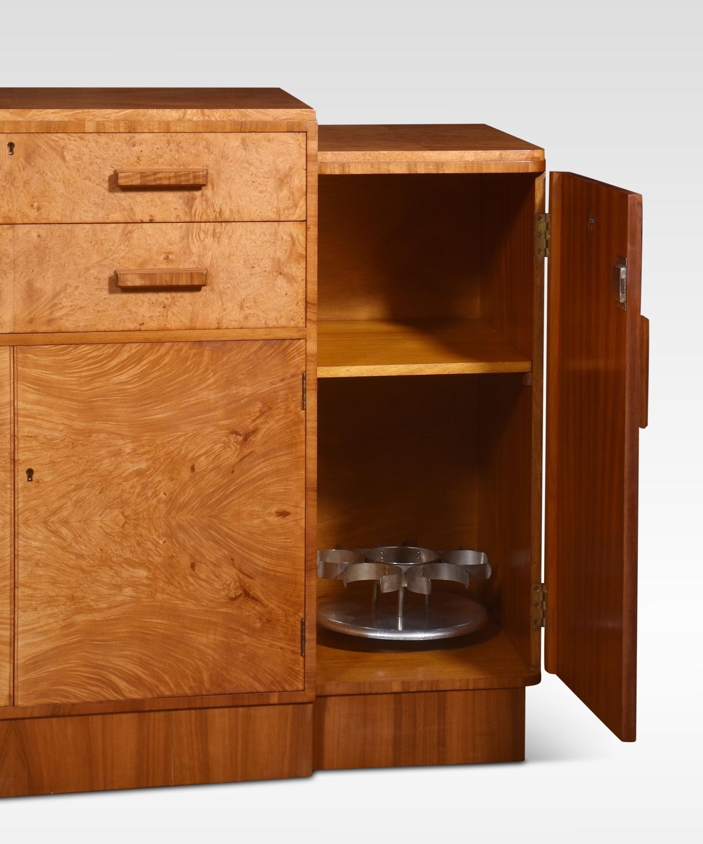 Art deco sideboard the well-figured walnut stepped top above two large central drawers with stylised handles, having two cupboard doors below opening to reveal a large storage area. Flanked by two further cupboard doors one fitted with a Crome