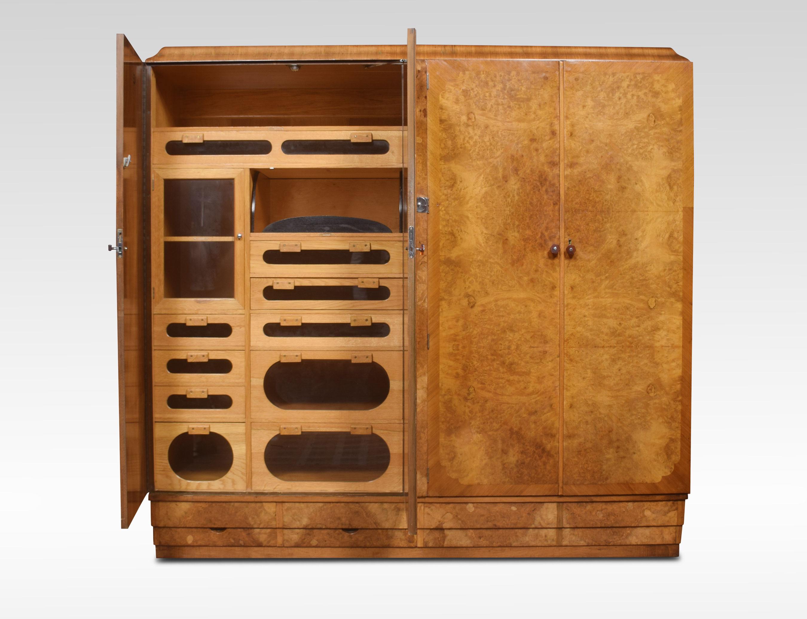 Walnut Art Deco compactum wardrobe, the moulded cornice above four two large doors with Bakelite handles, opening to reveal fitted glazed compartments, drawers and hanging space. All raised up on a plinth base fitted with two