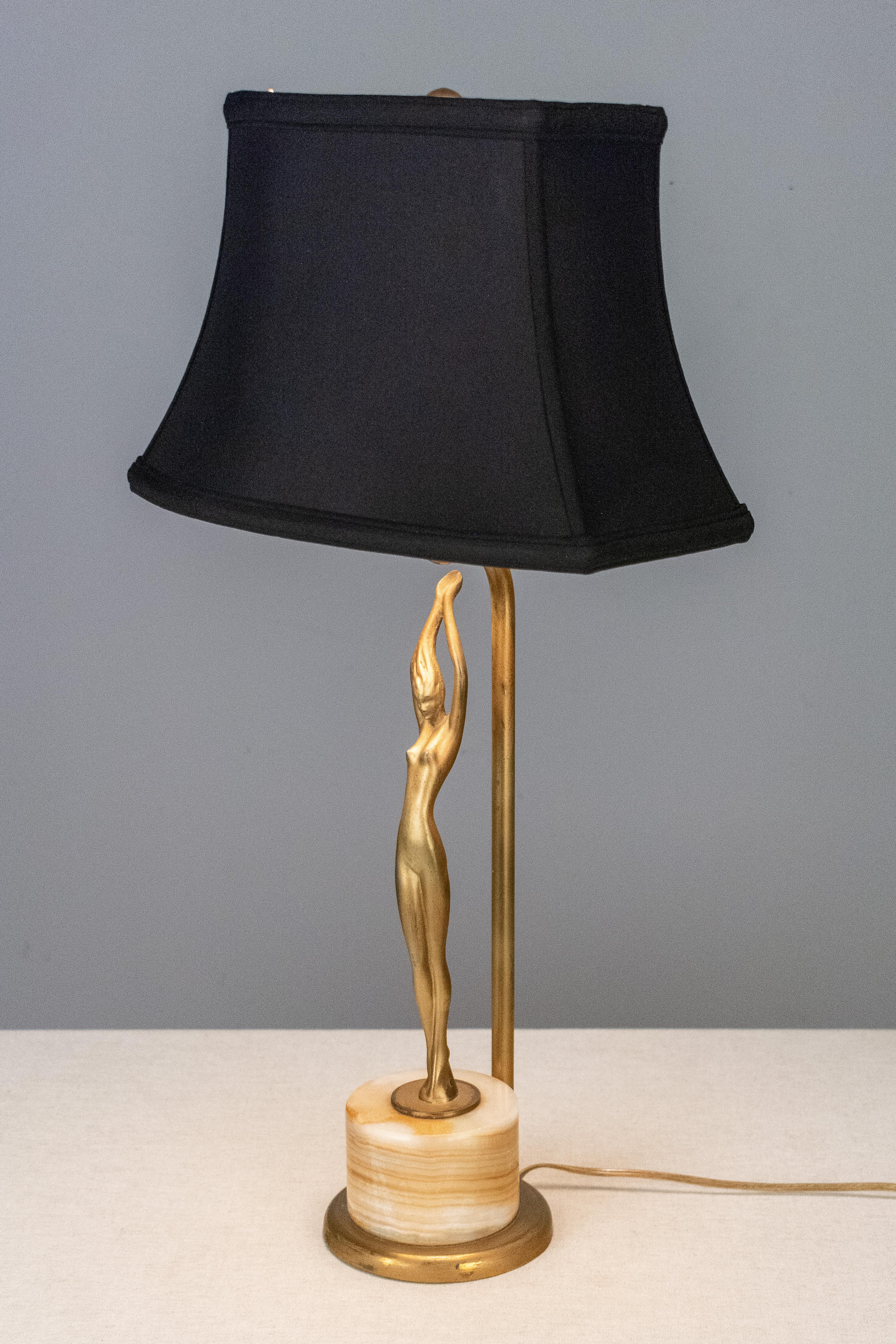 An American Art Deco lamp by Frankart, Inc. of New York depicting a svelte nude figure, arms upstretched to bask in the light above. Made of cast white metal with gold painted patina on an alabaster base. New black silk shade with gold lining