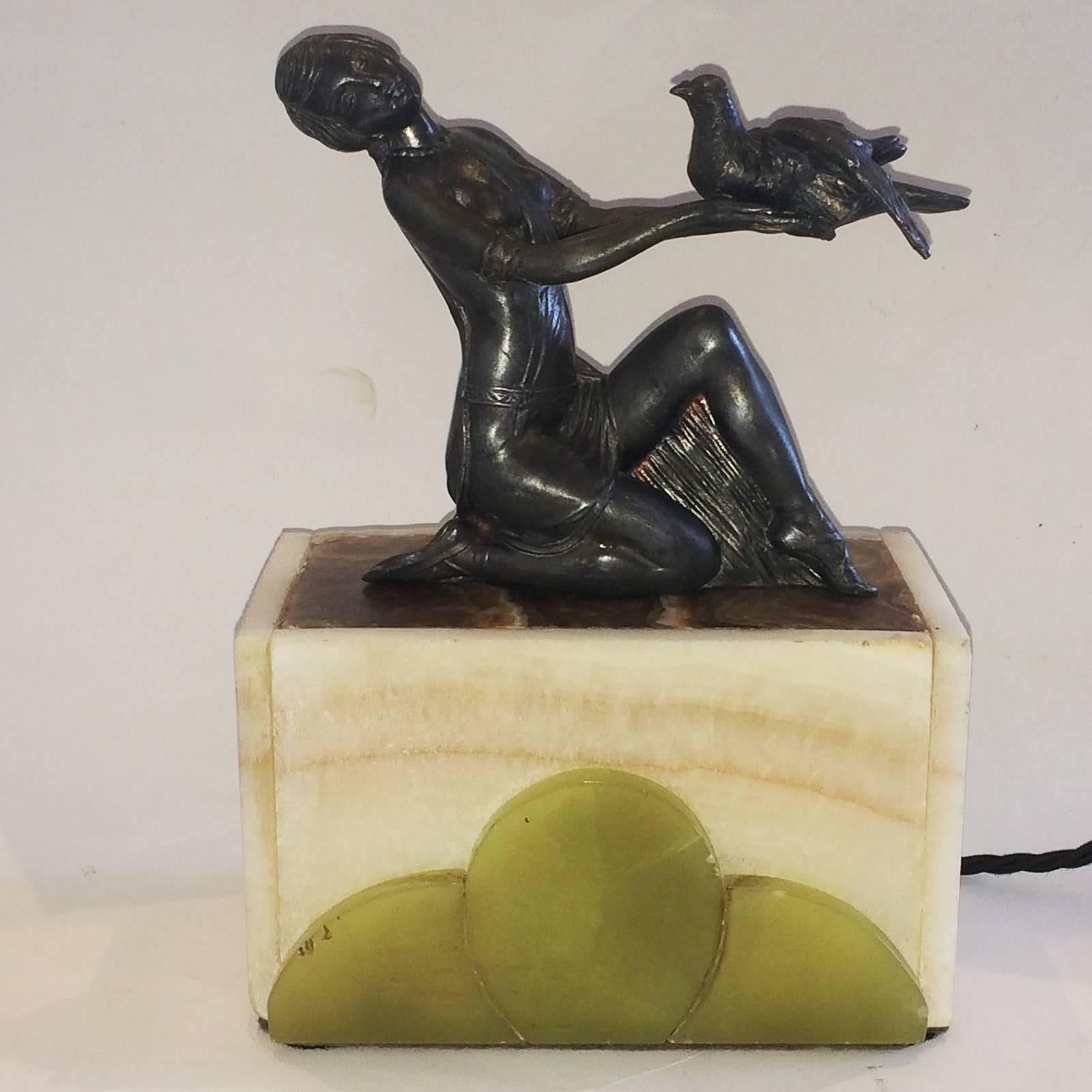 Art Deco lamp designed with a light box of two different Alabaster colors, including the green, carved geometric pattern section on the front. The metal statue above, is a Lady holding a Dove. When turned on, the lamp base glows all-over,