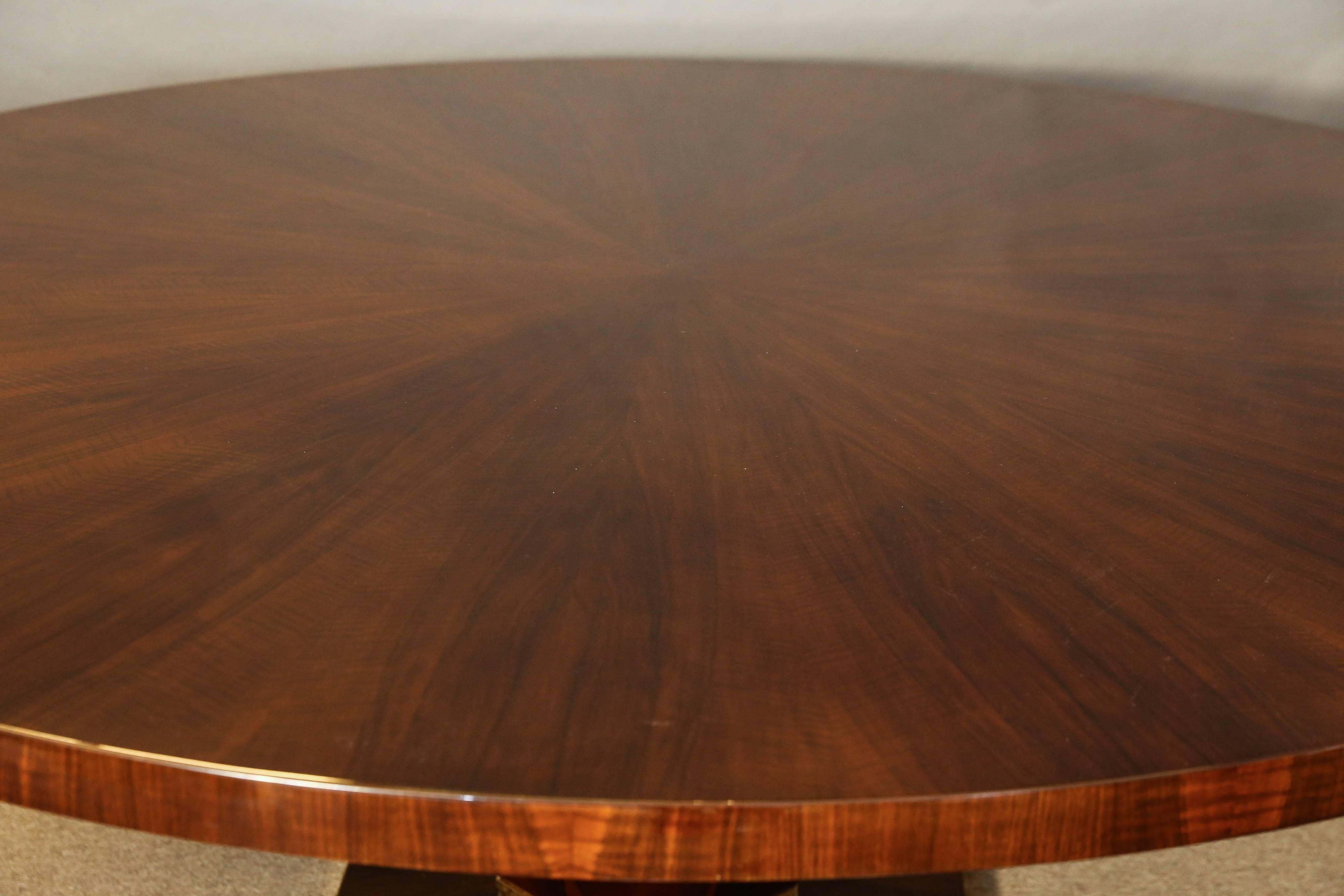 Beautiful dining room table is made out of fine walnut wood. Ttabletop is displaying radiant design of the wood panels. It rests on the wide prominent leg, that is supported by the octagonal base. The base is surrounded with a brass