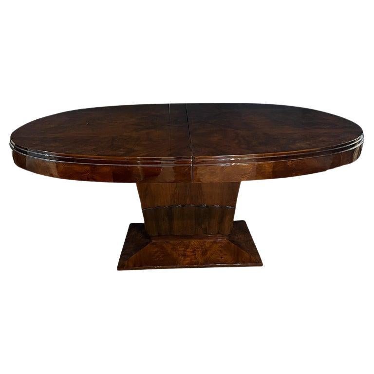 Il piano ovale del tavolo da pranzo mette in mostra la bellezza del legno di noce burlato. È sostenuta da una gamba ampia e prominente, che poggia su una base rettangolare. La parte inferiore della gamba di sostegno presenta un intaglio decorativo