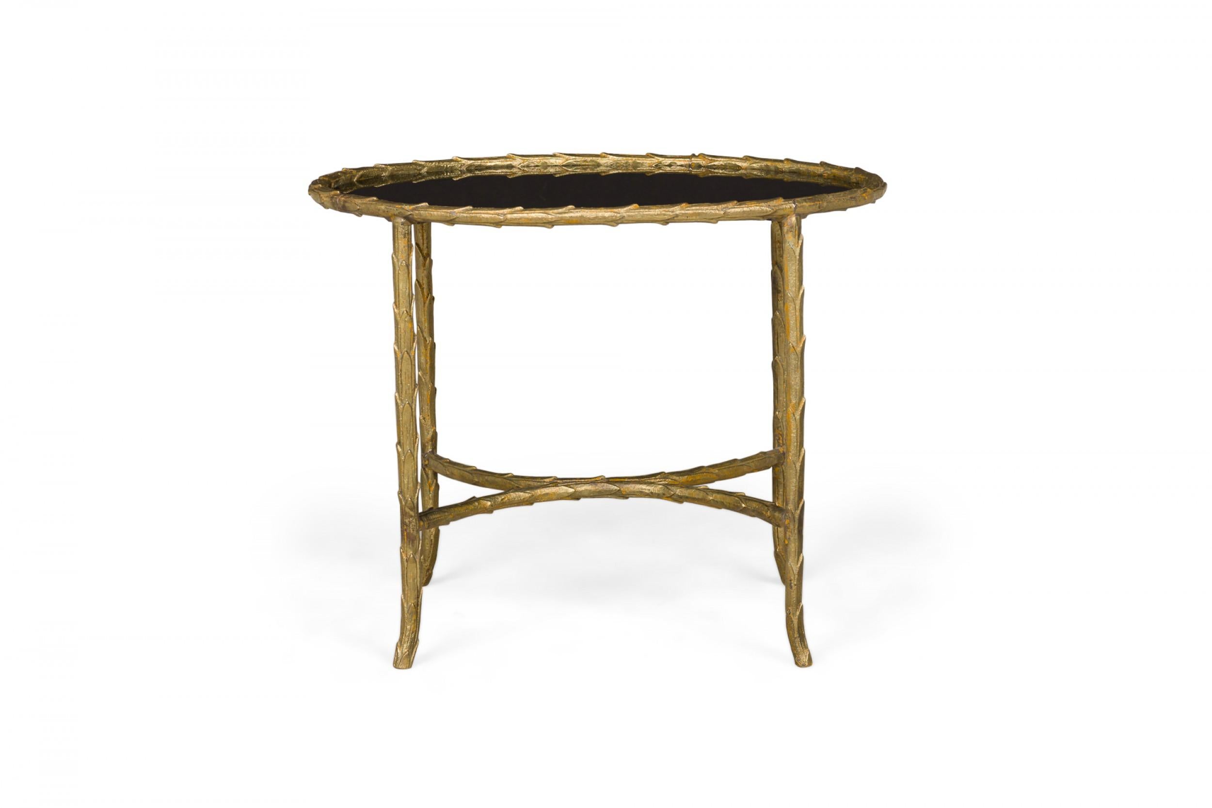 Art Deco French oval-shaped end / side table with an opaque black glass top inset into a molded bronze frame in faux bamboo form with opposing demilune stretchers, standing on four legs with slightly curved feet.
