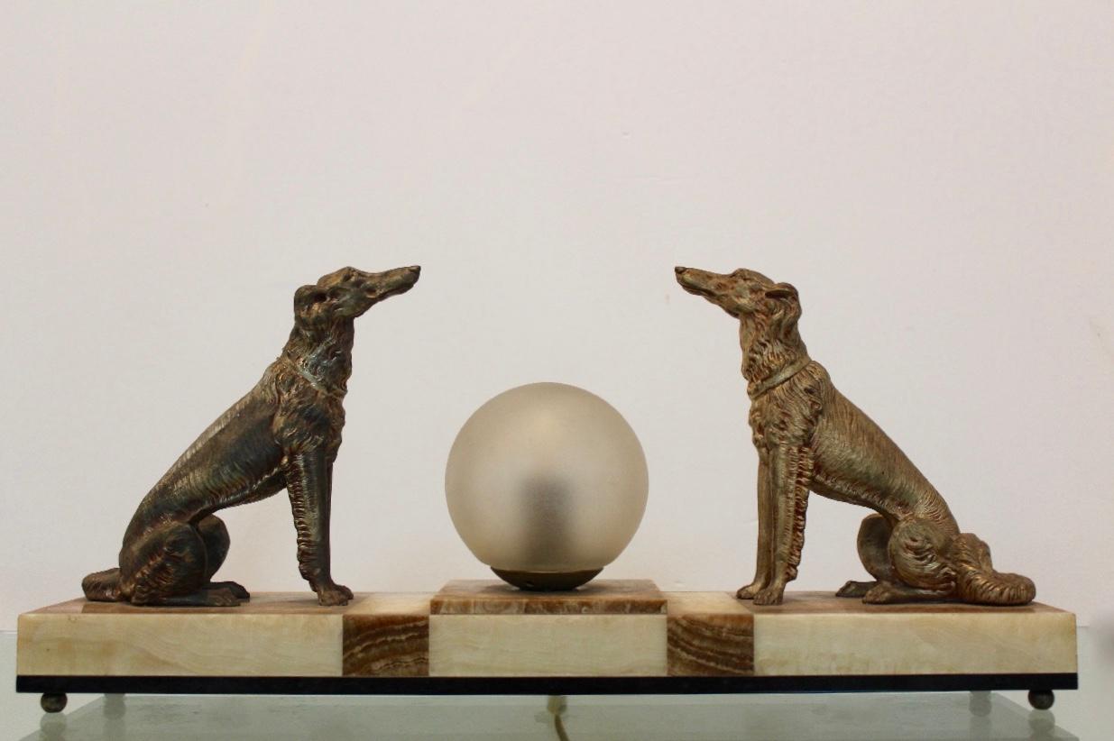 Sophisticated and Chique Art Deco French Greyhound sculpture Table lamp. In silvered and patinated metal depicting two greyhound dogs with in the middle a glass round opal glass bulb. The figures stand on a rectangular marble and alabaster base.