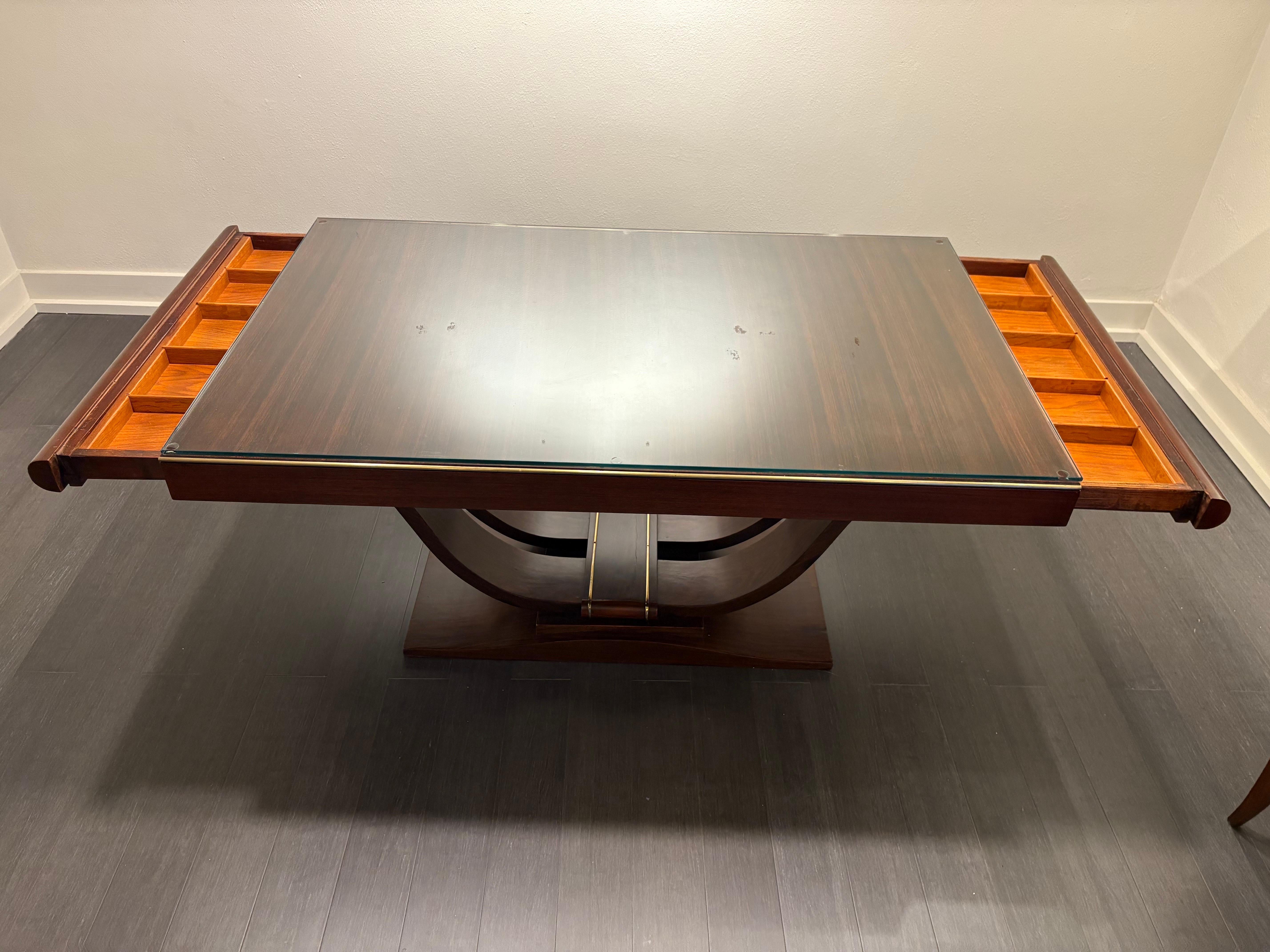 A great table harkening back to the deco period with its simple design yet sophisticated execution. The swooping pedestal offers timeless elegance complemented by the polished mahogany and brass piping along the sides. Each end conceals a drawer