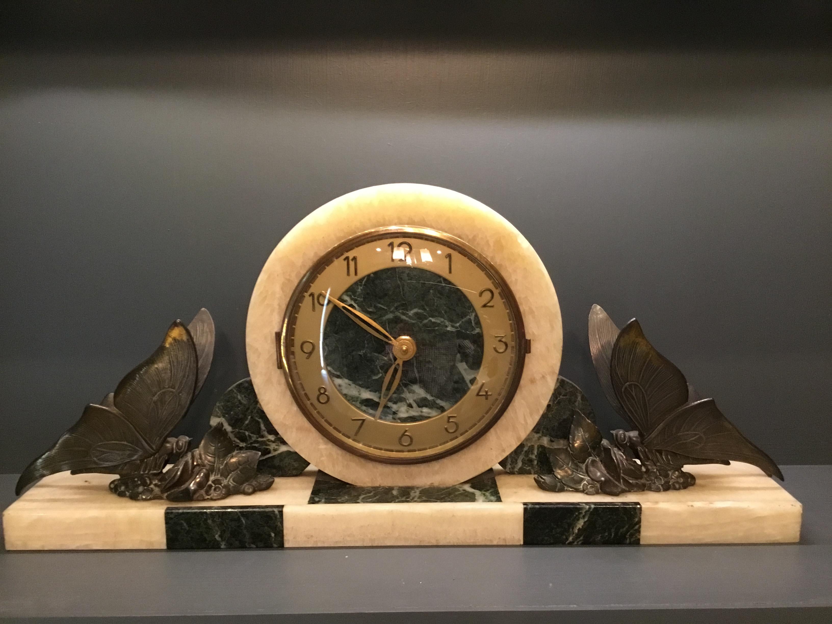 Art Deco French mantel clock with two garnitures of grey and cream marble.
The clock has brass hands and Art Deco style numerals and is particularly appealing due to the cast butterfly’s mounted to each end of the clock.
A lovely addition to any