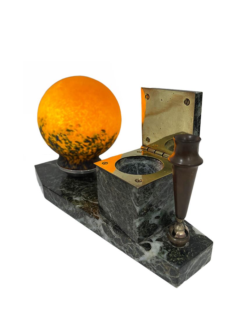 Art Deco French marble inkwell with lamp, 1920

A marble inkwell with hinged lid on a marble base with a pen holder made of bakelite and a small round “Pâte de Verre” glass lamp shade, signed. Orange with blue glass. The lampshade is clamped on a