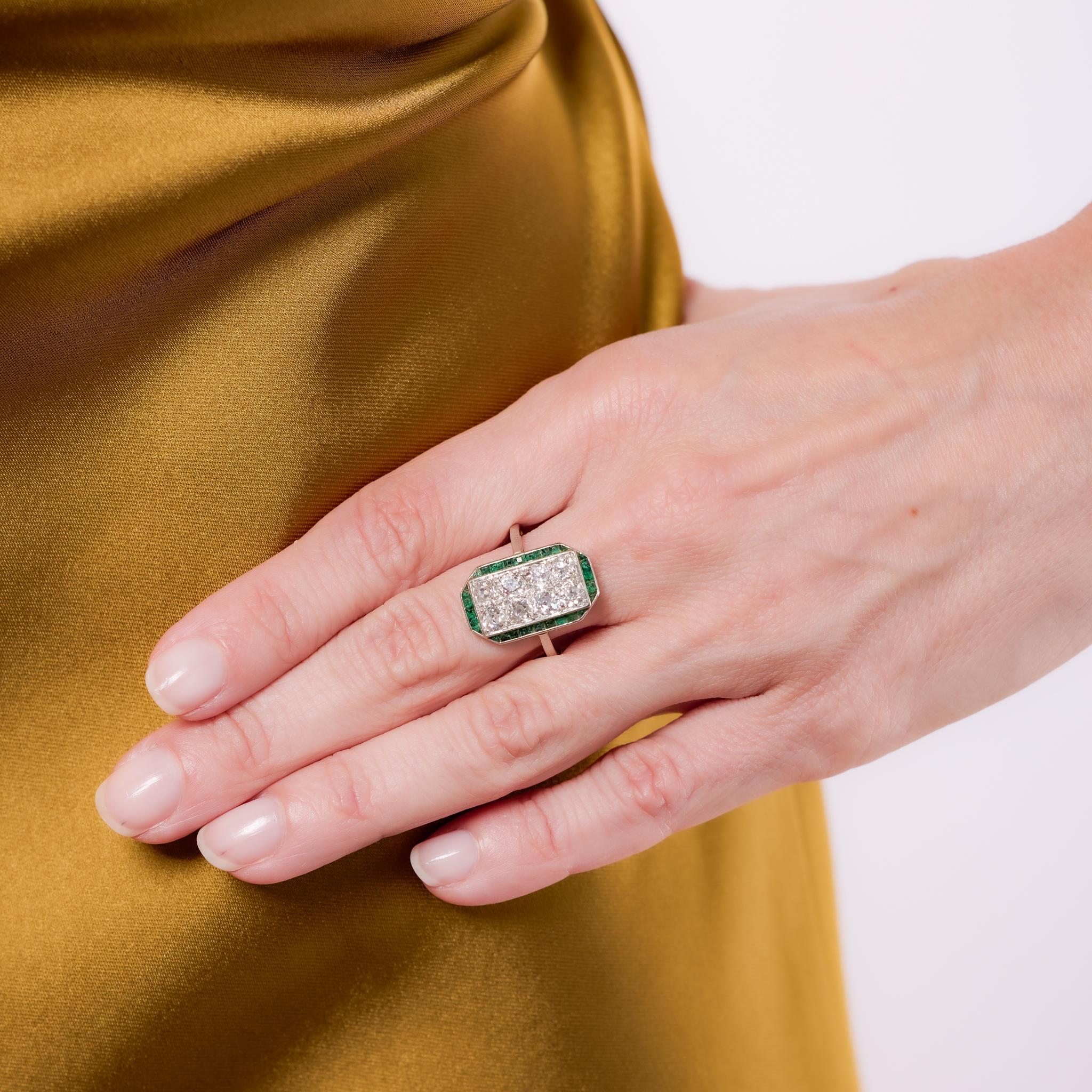 Crafted in the 1930s, this French Art Deco ring showcases a striking combination of 8 old mine cut diamonds totaling approximately 1.80 carats, graded G color and SI clarity. Framed by 28 calibre cut emeralds totaling approximately .40 carats, the