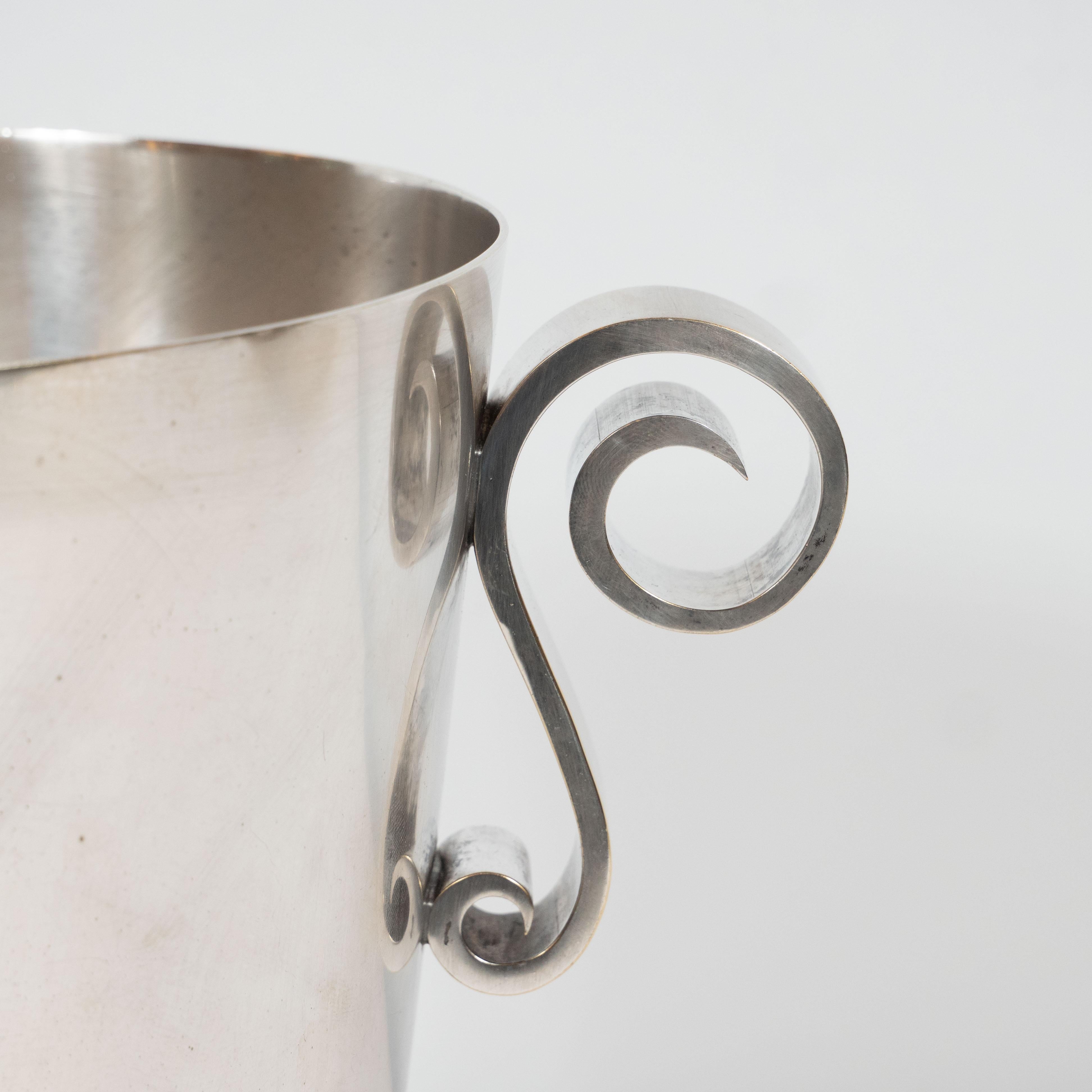 This French Art Deco silver plated ice bucket was produced circa 1935. A series of stacked pleats circumscribe the perimeter of the base of the ice bucket creating a dynamic profile. The top half of the bucket is left unadorned except for two