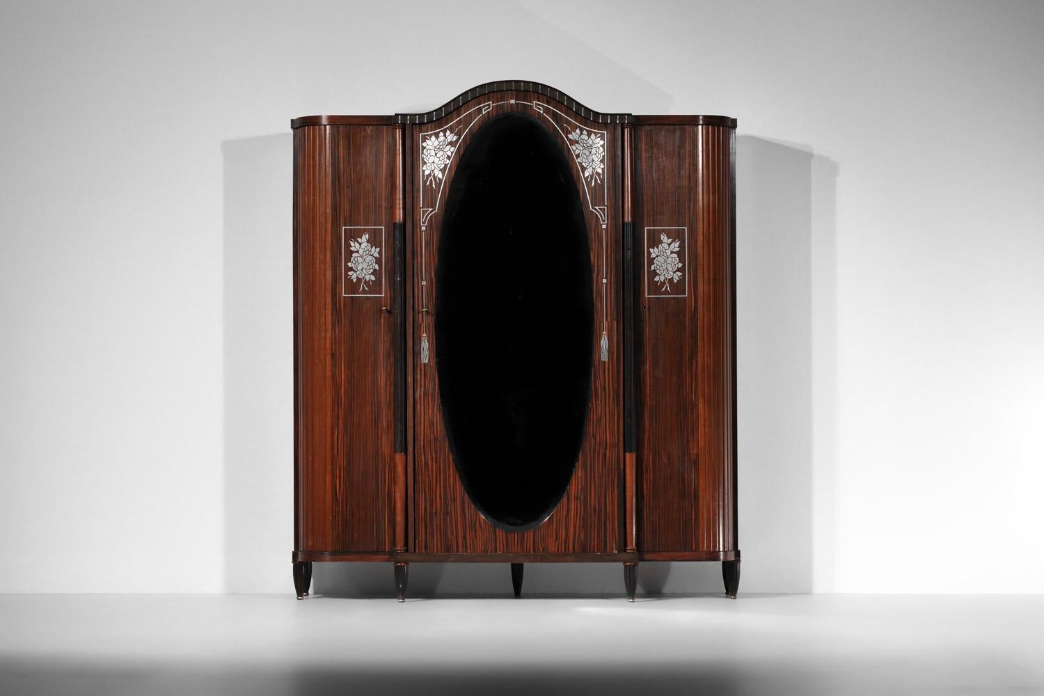 Large 1930s art deco wardrobe in the style of Maurice Dufrène. 
This armoire has two hinged side doors opening onto a series of shelves and a central door with a large mirror opening onto a wardrobe. 
Very nice decorative work with marquetry using
