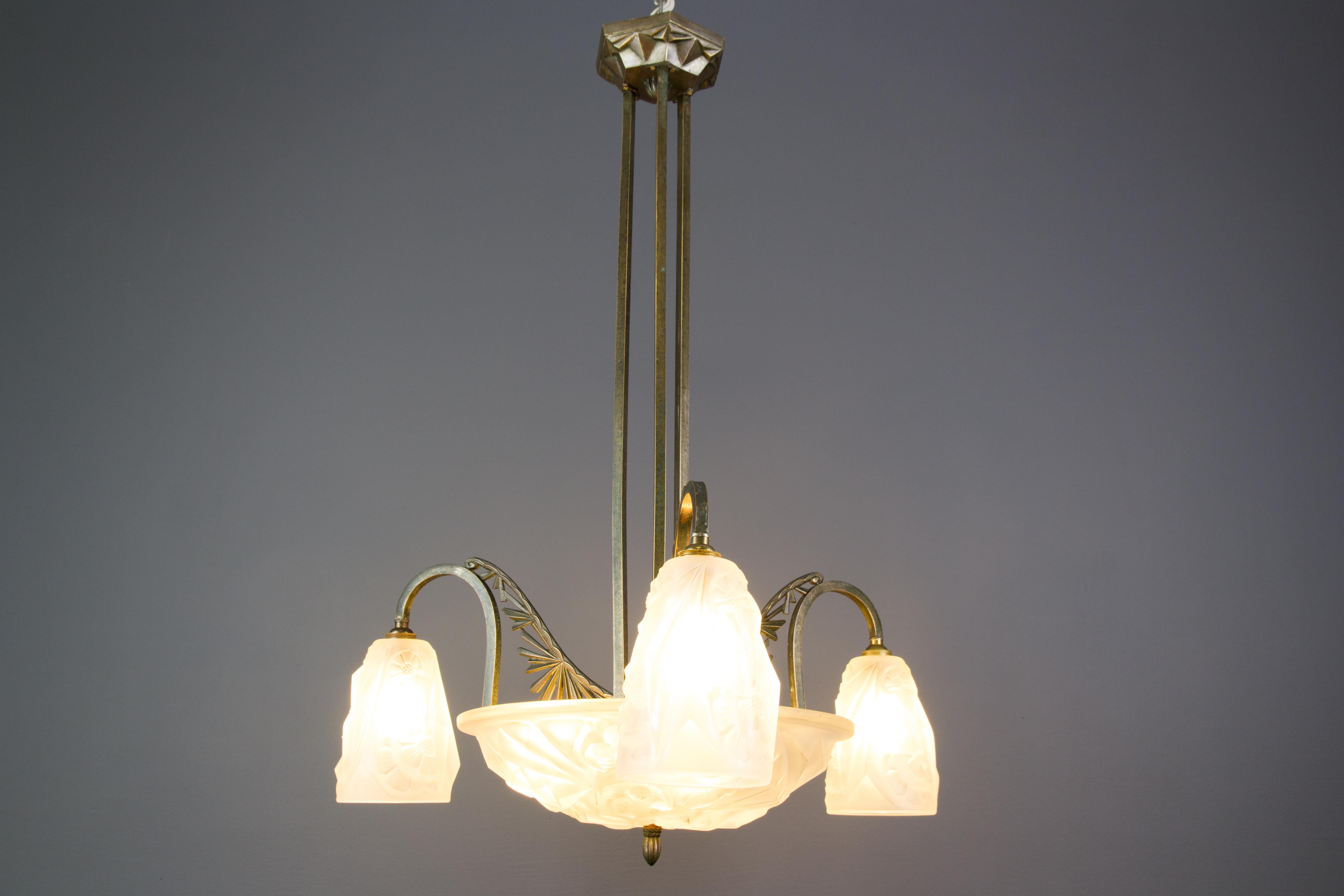 This beautiful French Art Deco six-light chandelier features white frosted molded-pressed glass shades with stylized flower motifs and an elegant bronze frame with three branches, decorated with geometrical Art Deco style elements. The glass shades