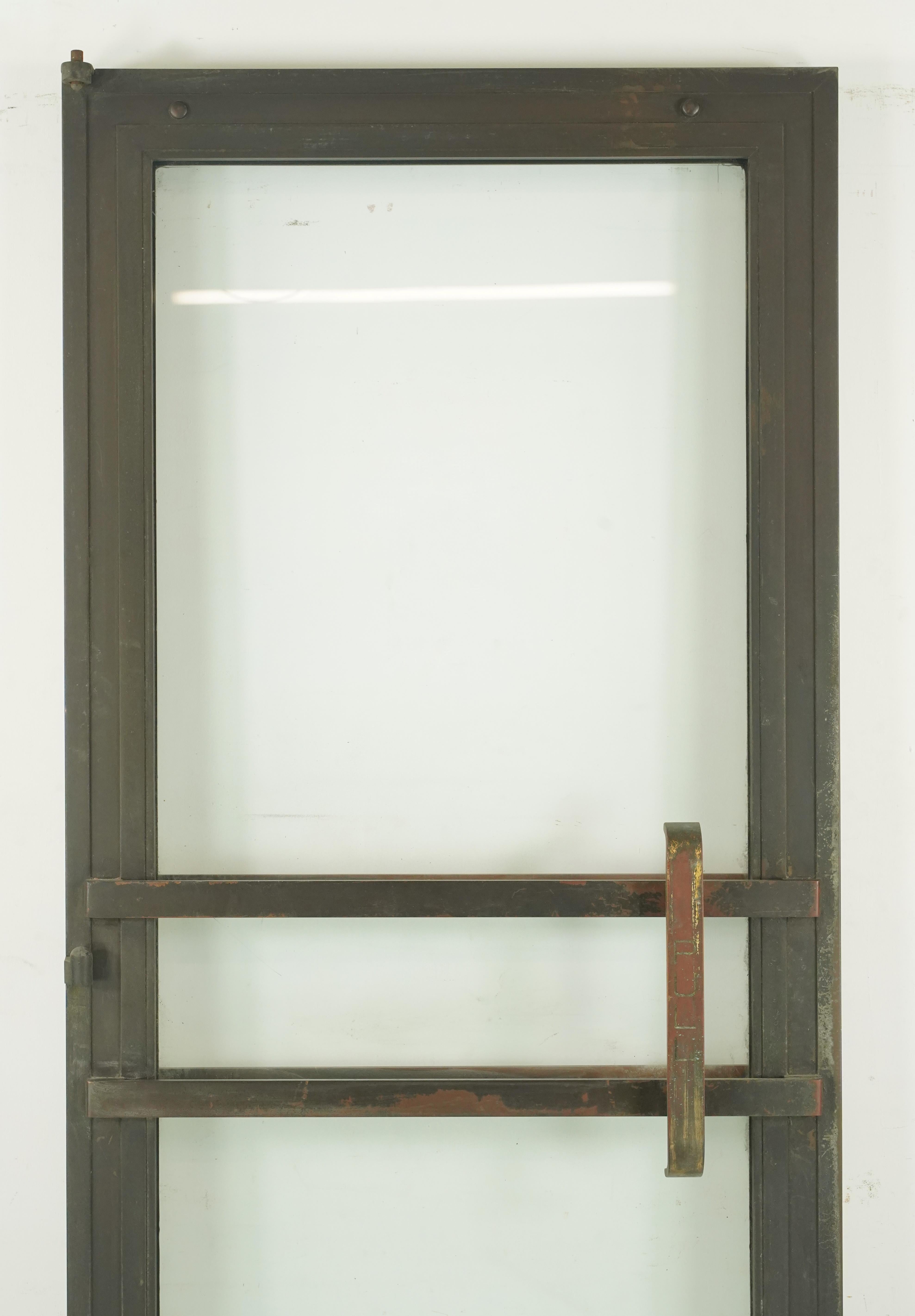 Art Deco commercial right hand out swing bronze frame door with a full glass panel. The hinge pockets are made of steel. The pull bars are made of brass. Good condition with surface wear and a cracked glass from prior use. Please note, this item is