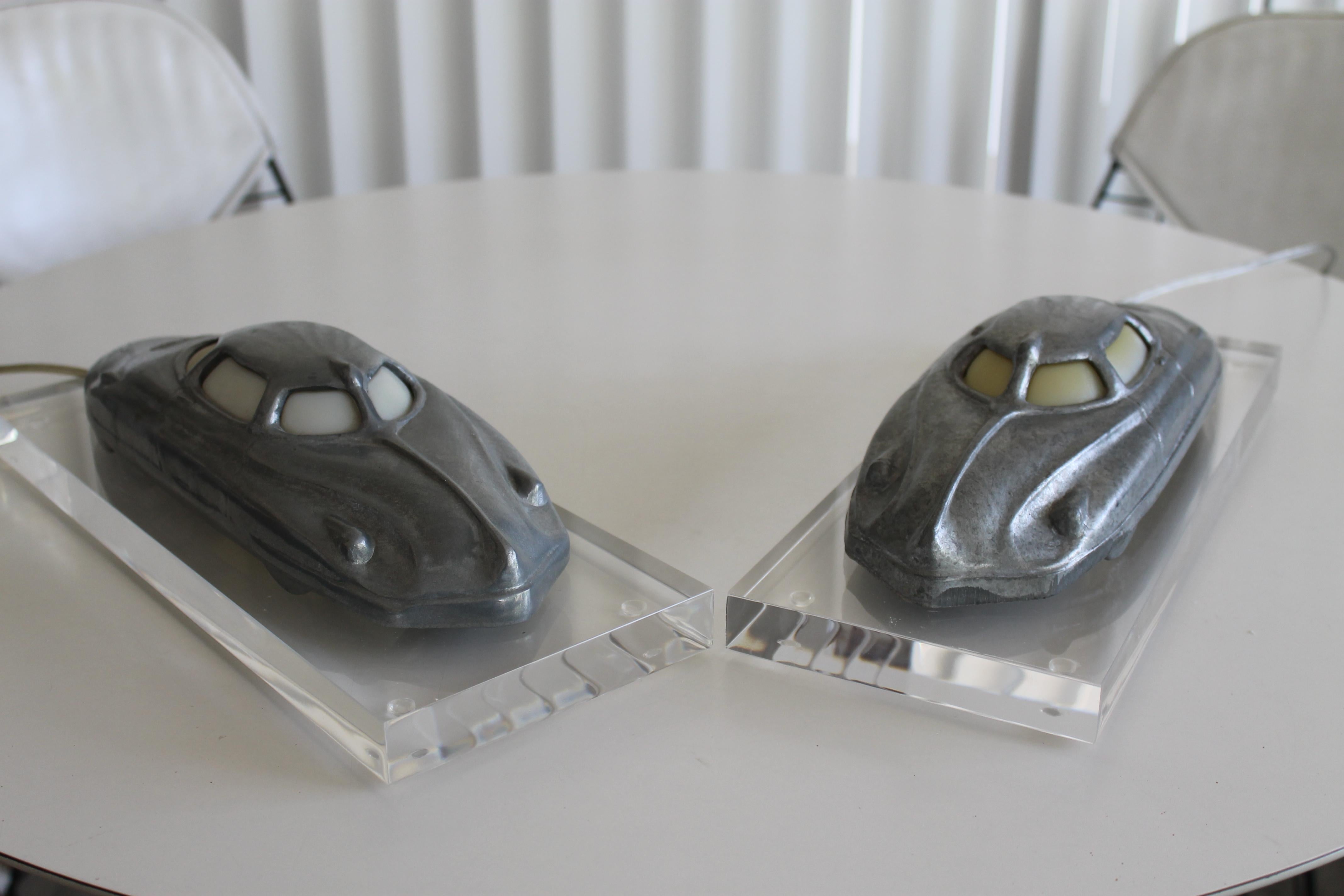 A pair of cast aluminum futuristic automobile lamps circa 1980's. These were recast from the original and extremely rare 1948 Playmate Toys pull toy. Each has a custom made clear lucite rectangular base measuring 14.5