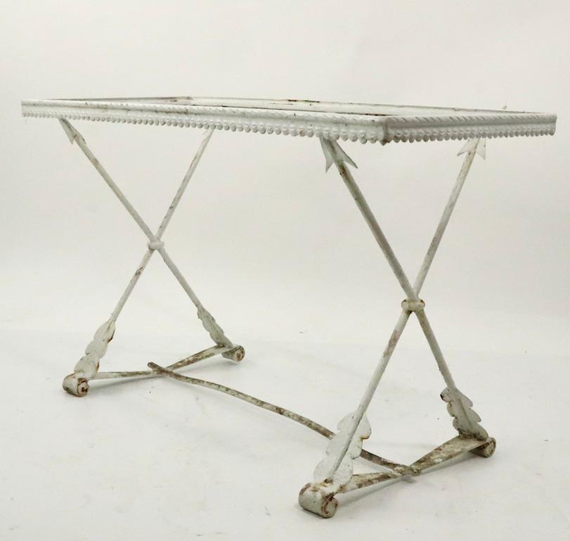 Unusual Art Deco wrought iron table having classical X-form arrow base, with glass top. Currently in older white paint finish, glass top has damage, top is easily replaced if you want a more finished look. Possibly Salterini, or Leinfelder, unsigned.