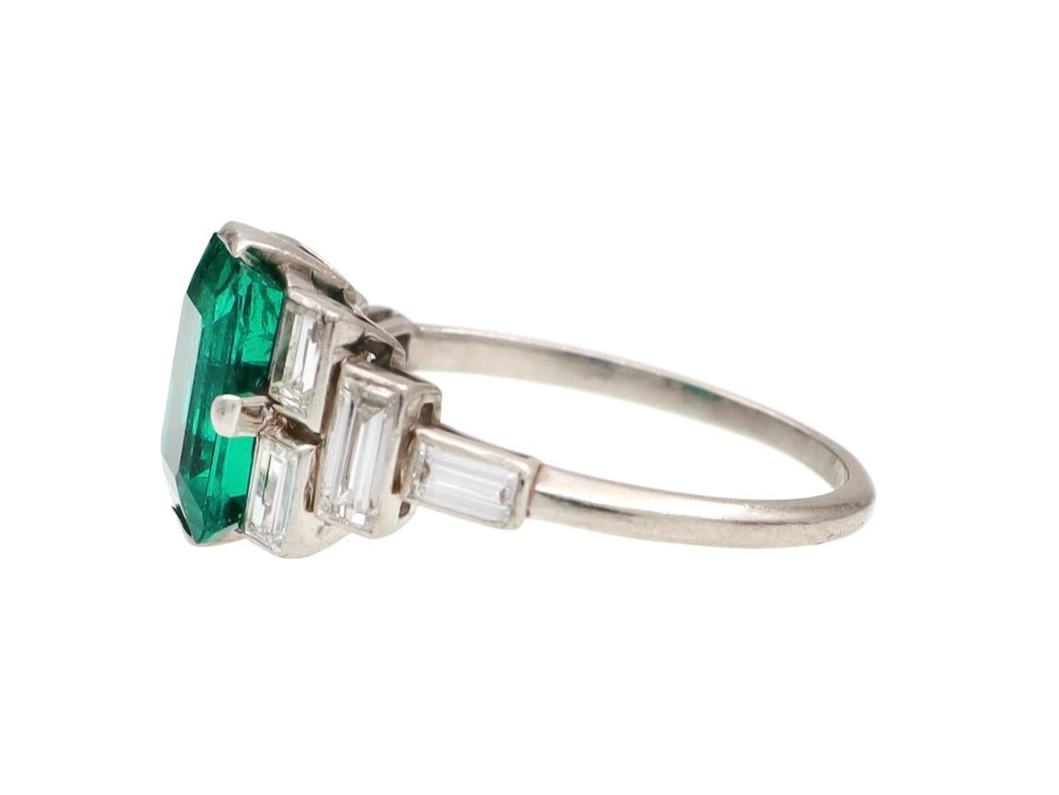 Art Deco Colombian emerald and baguette diamond ring in platinum. Set with an estimated 1.75ct octagonal emerald cut Colombian emerald with minor clarity enhancement in four claw compass setting, flanked to either side with eight rectangular