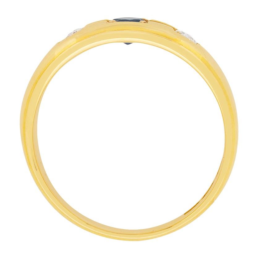 Realizzato nel 1927, questo splendido anello da uomo in oro giallo 18 carati presenta uno zaffiro blu intenso incastonato tra una coppia di diamanti taglio vecchio, tutti incastonati a griffe in montature a scatola aperta all'interno di una cresta