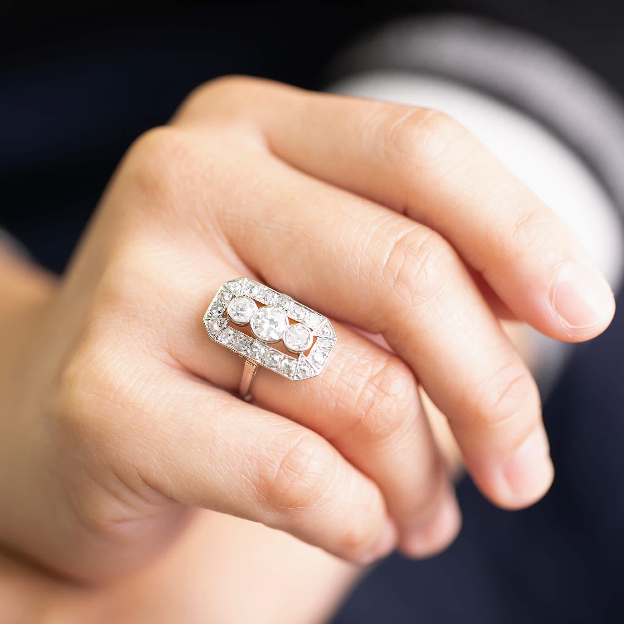 Art-Deco-Diamant-Cluster-Ring aus Platin. Das Fahrgestell ist mit schönen Schnörkeln versehen. Trueing seiner Zeit entsprechend, ein  Die mit Diamanten besetzte, gefräste, geometrische, achteckige Form umrahmt drei Diamanten in der Mitte der Lünette