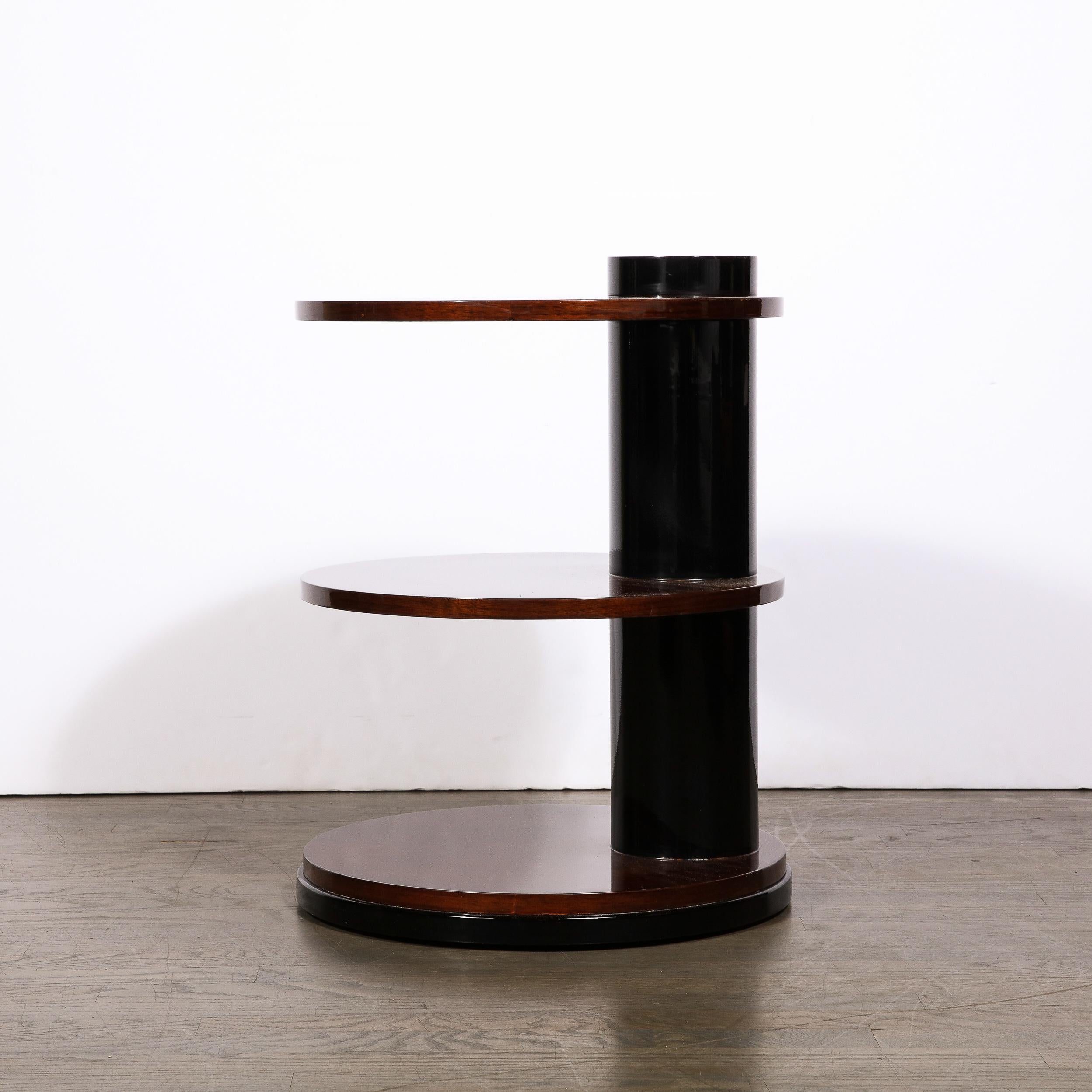 This graphic and elegant Art Deco Machine Age occasional table was realized in the United States circa 1935. It features three evenly spaced round tops in beautiful bookmatched black figured walnut that are pierced through by a lustrous black