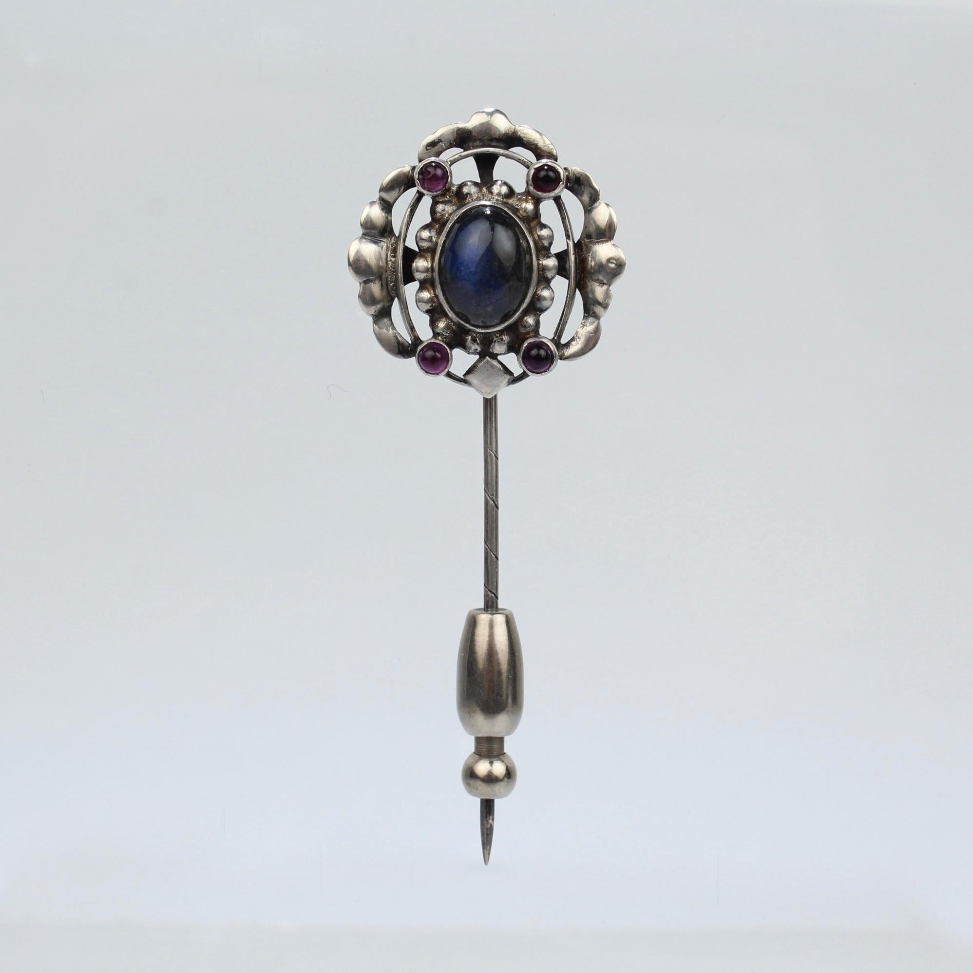 A rare Georg Jensen silver stick pin.

Model no. 17. 

Set with a central Labradorite cabochon and four small amethyst cabochons. (And accompanied by an added safety slide for extra security).

Dates between 1917 and 1927.

A rare early Jensen piece