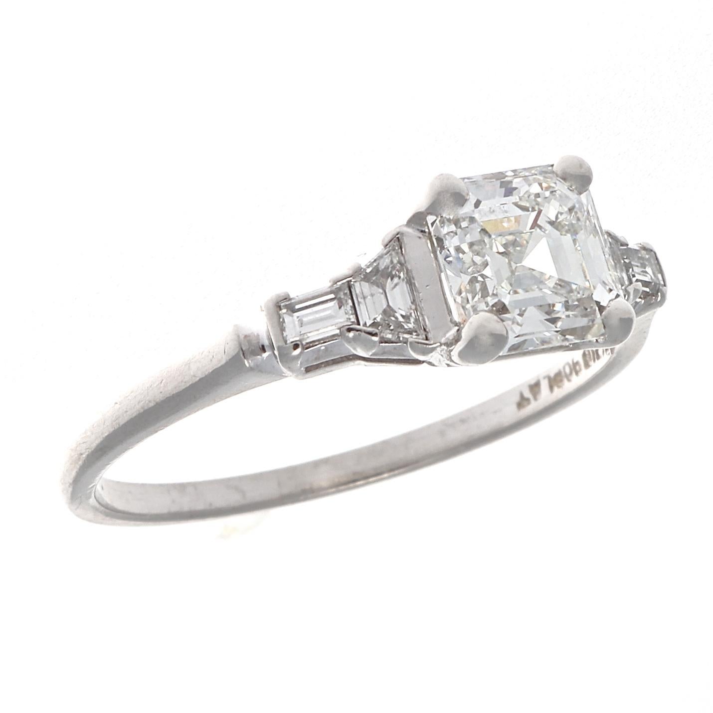 An eternal symbol of longevity with your partner in life. Featuring a 1.03 carat Asscher cut diamond that is GIA certified as G color, SI1 clarity. Accented by trapezoid cut  and baguette cut diamonds on either side. Crafted in platinum. Ring size